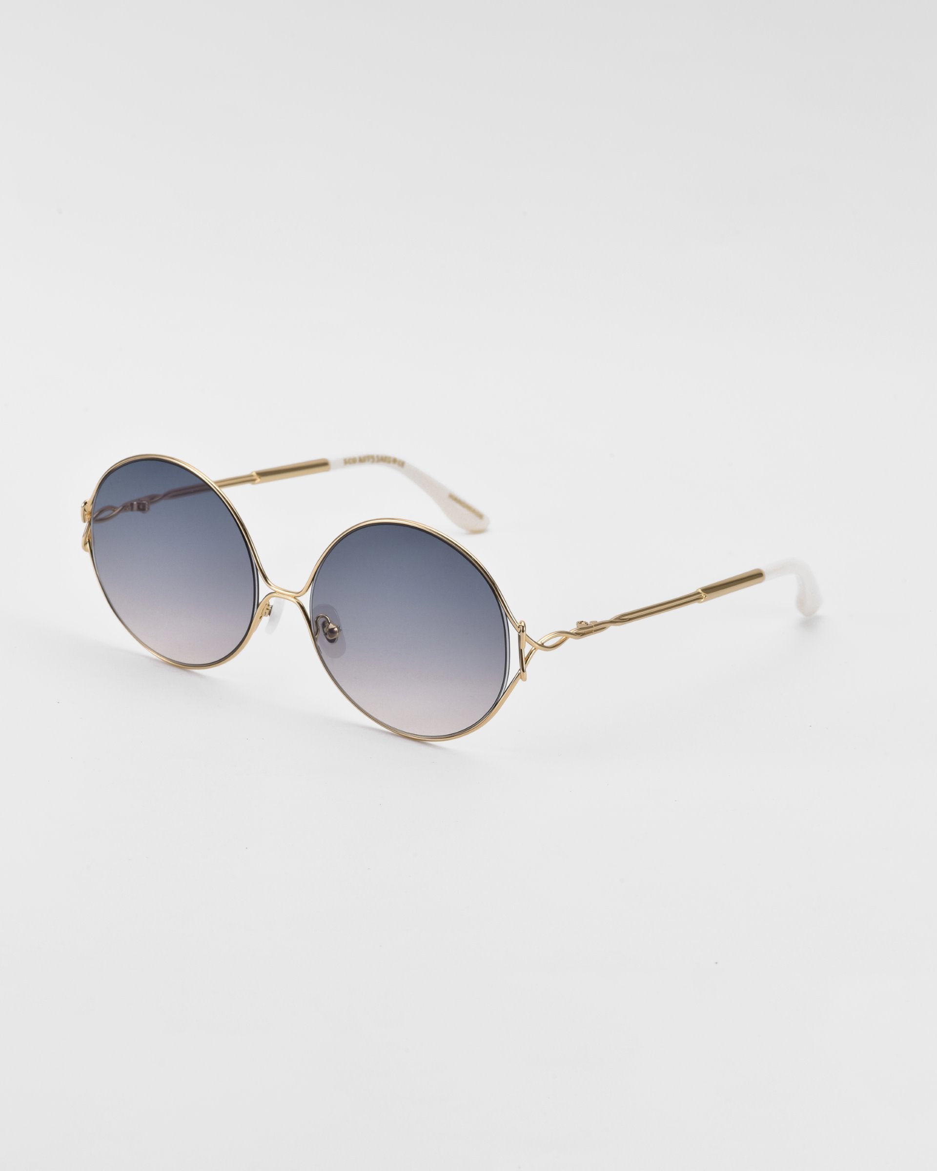 A pair of retro-inspired Aura sunglasses by For Art&#39;s Sake® with oversized round frames in gold metal and gradient blue lenses. The Aura sunglasses have thin temples with white tips and a minimal design against a plain white background.