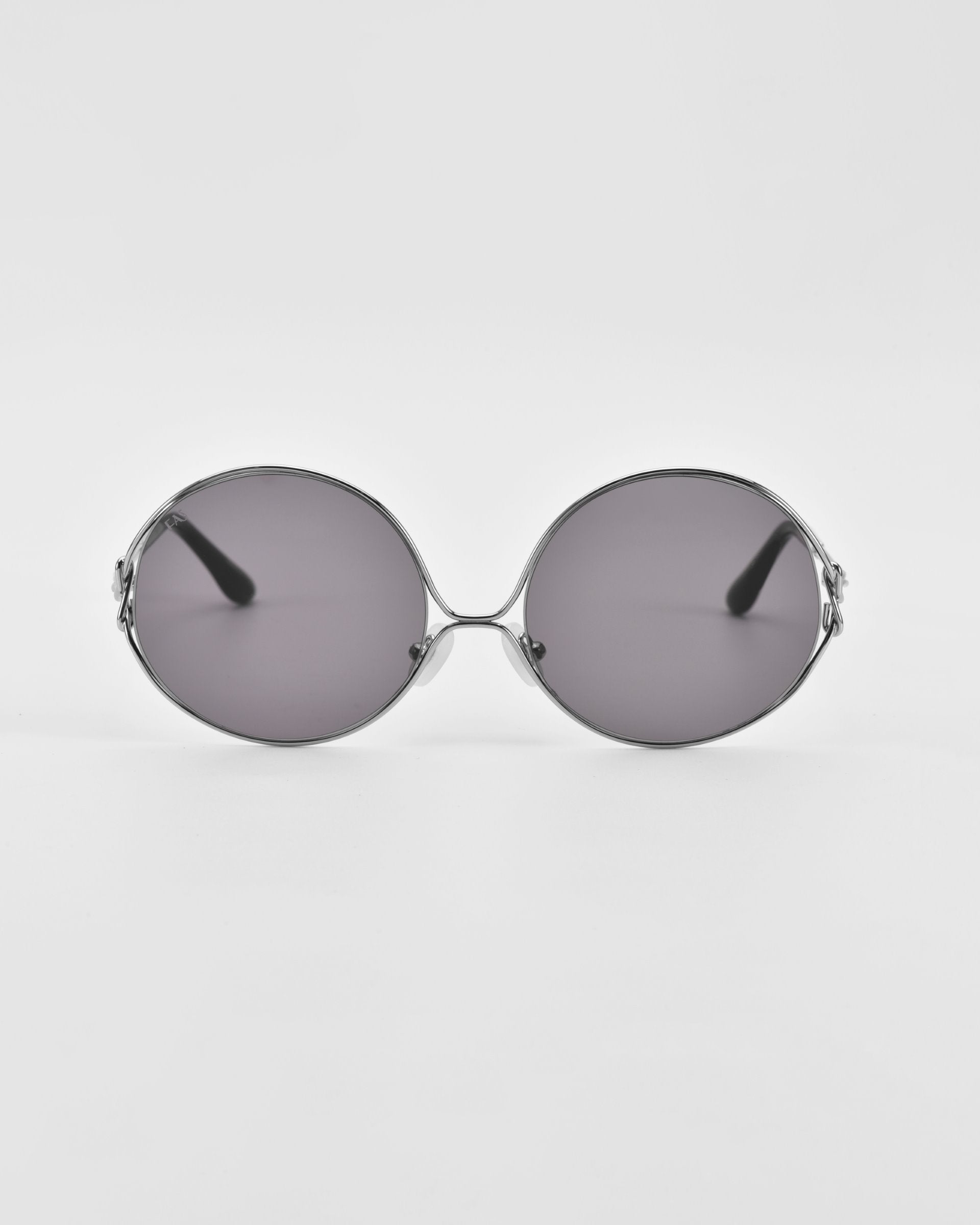A pair of Aura sunglasses by For Art&#39;s Sake® with gradient tinted lenses and thin, silver-colored metal frames. The oversized round frames extend backward, offering a sleek and minimalist design. The sunglasses are set against a plain white background.