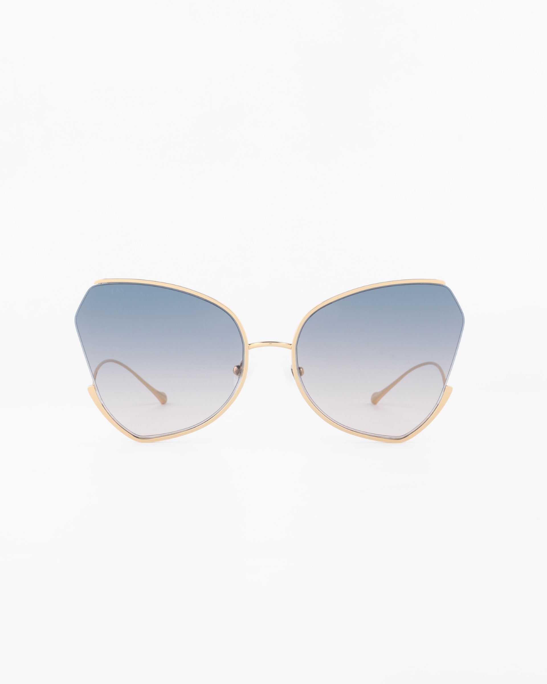 Close-up of a pair of Watercolour sunglasses by For Art&#39;s Sake® with gold-plated stainless steel frames and large, gradient blue lenses. The glasses have a sleek, modern design with slightly geometric lenses, offering UV protection. The background is a clean, plain white.