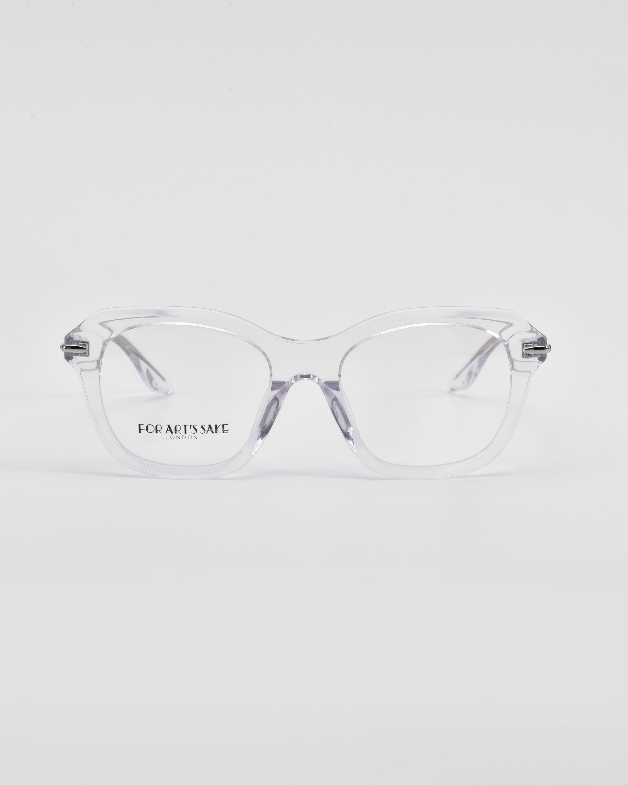 A pair of clear eyeglasses with transparent frames and a hint of a cat-eye silhouette rest on a white surface. The lenses have the text &quot;For Art&#39;s Sake® Helene&quot; printed on the left side. The design is minimalist and modern, with slightly thick frames and a subtle, elegant appearance.