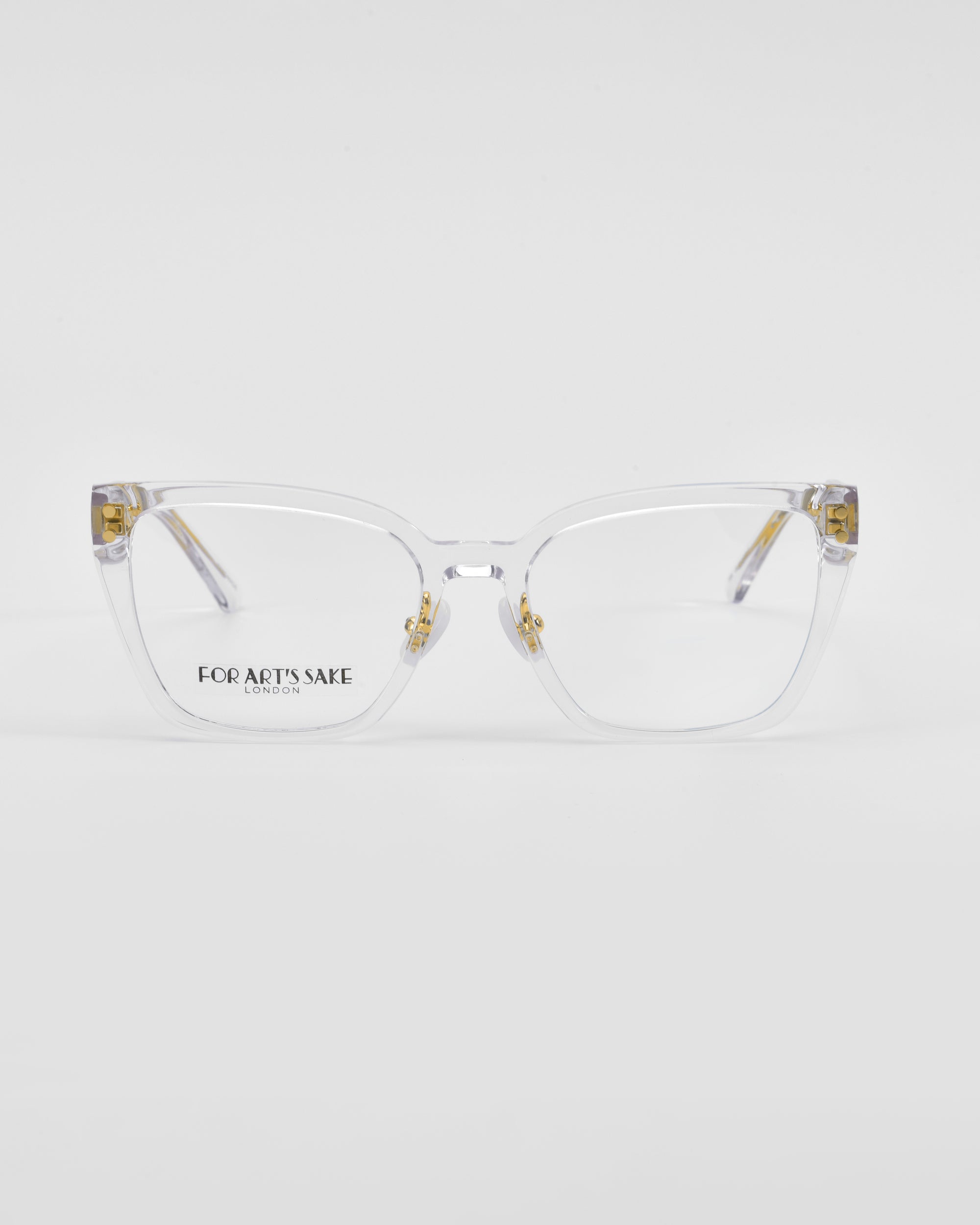 A pair of clear-framed Abbey eyeglasses with slightly oversized square lenses. The temples have a hint of gold-plated detail, and the brand For Art&#39;s Sake® is subtly printed on the inside of the right lens near the temple. The background is a plain white.
