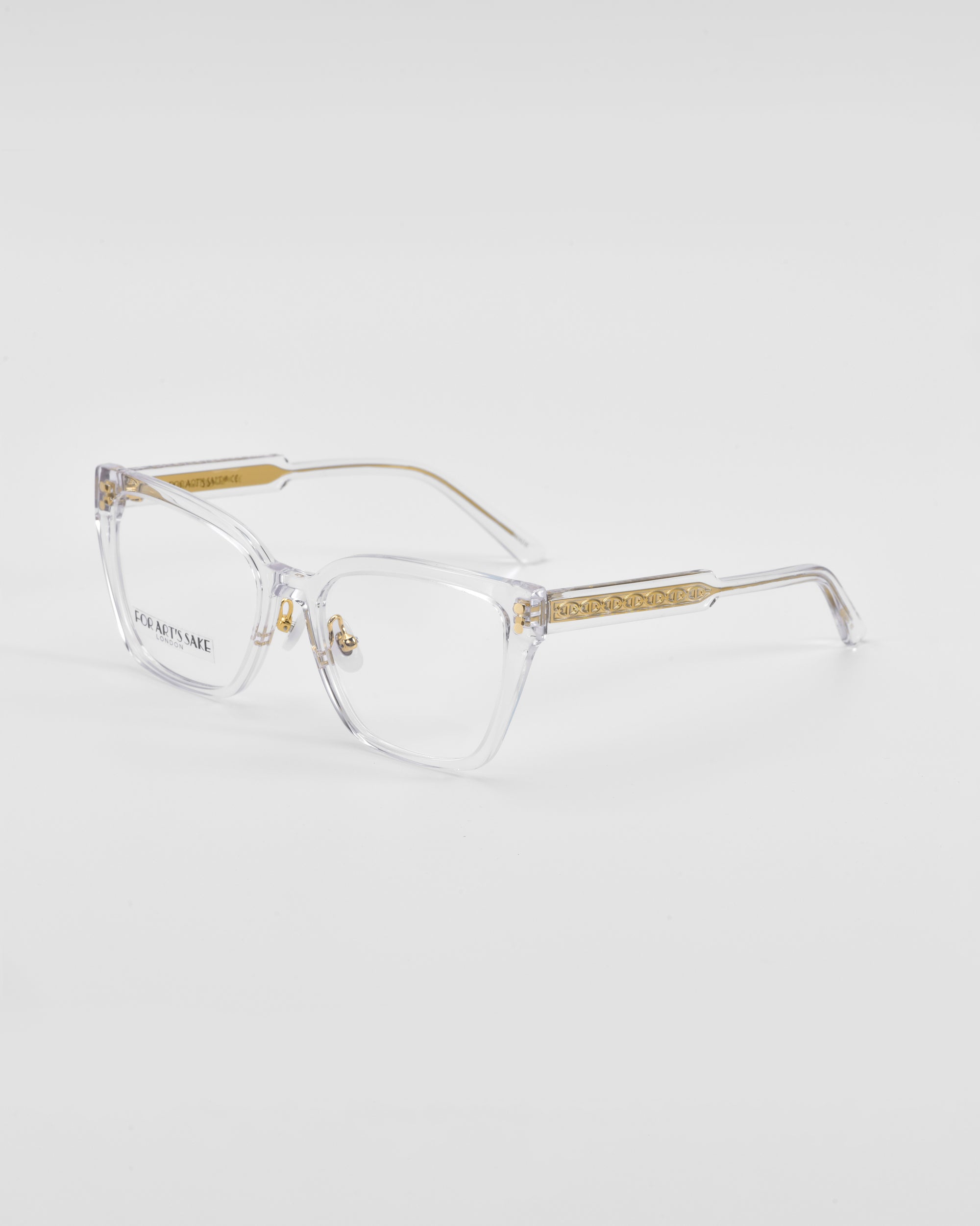 Abbey by For Art&#39;s Sake®: Clear cat-eye opticals with gold-accented temples, featuring a delicate link-chain pattern on the sides. The frames are transparent with a modern, minimalist design. The background is a plain, light grey color.