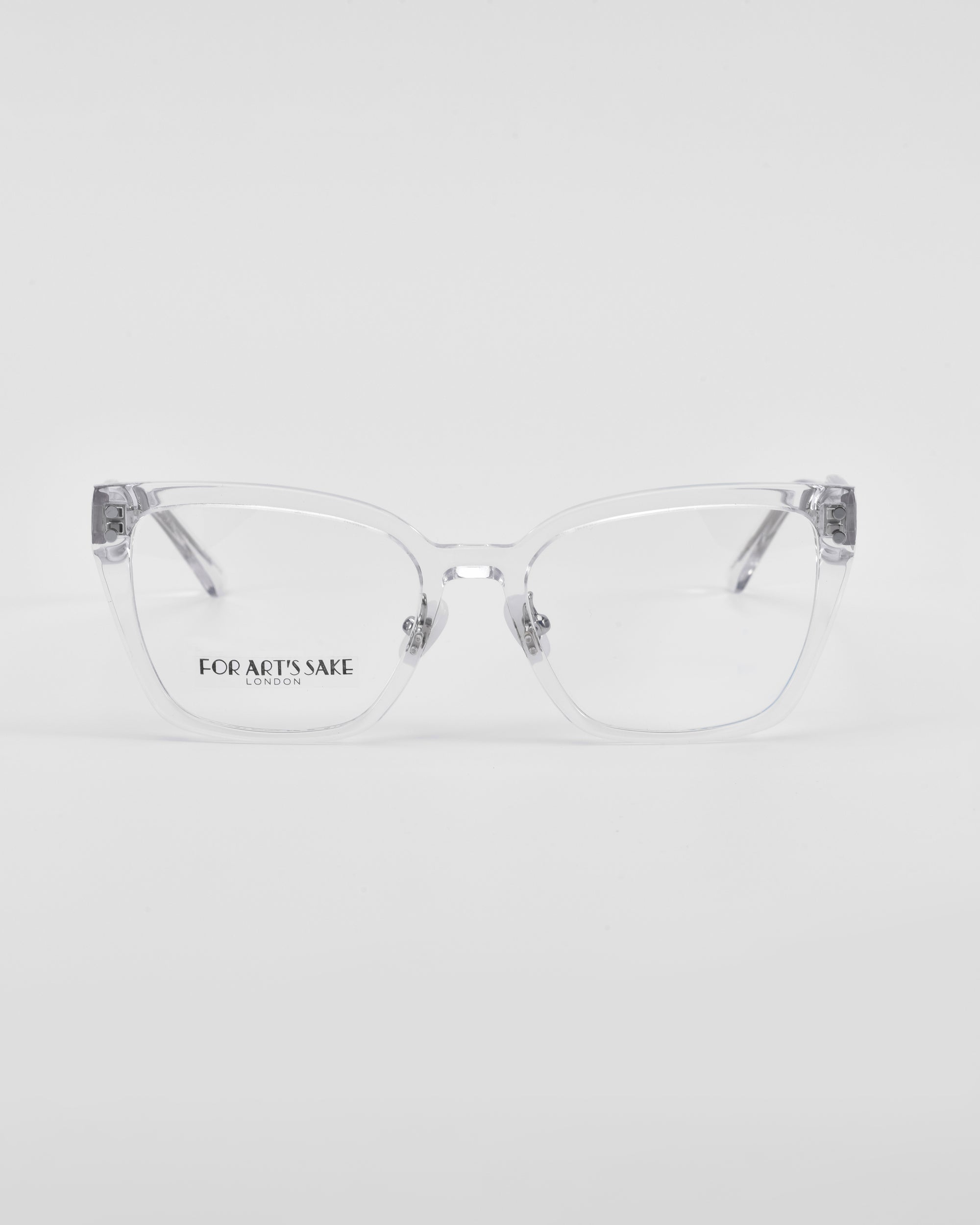 A pair of transparent prescription glasses with a minimalist design, rectangular lenses, and &quot;For Art&#39;s Sake®&quot; printed on the left lens. Featuring 18-karat gold-plated accents for an exquisite touch. The background is plain white.