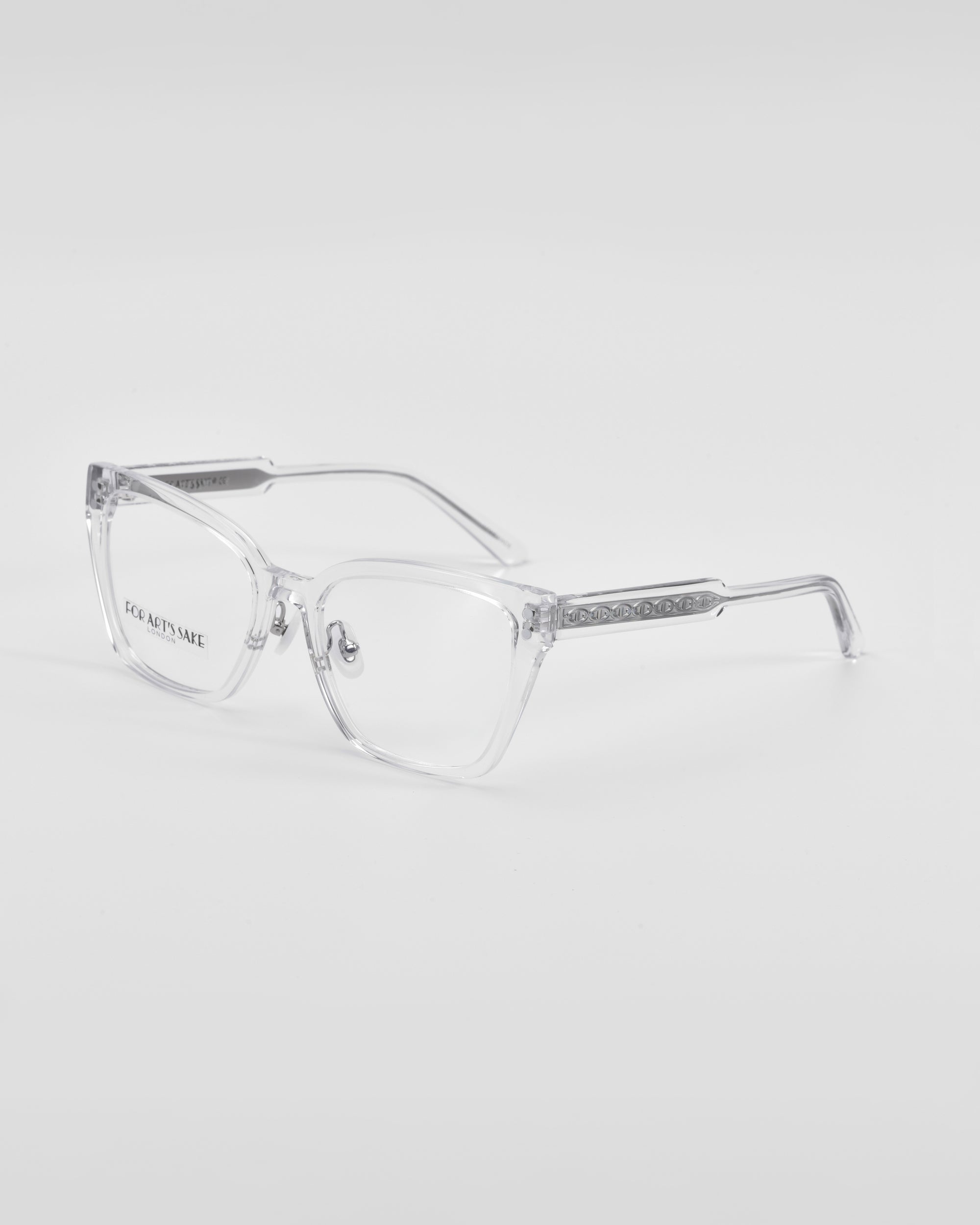 A pair of Abbey eyeglasses by For Art&#39;s Sake® with clear lenses. The eyeglasses have a sleek design with decorated arms featuring a subtle link-chain pattern and small, embedded stones. The brand name &quot;For Art&#39;s Sake®&quot; is visible on the inside of the left temple. The background is plain white.