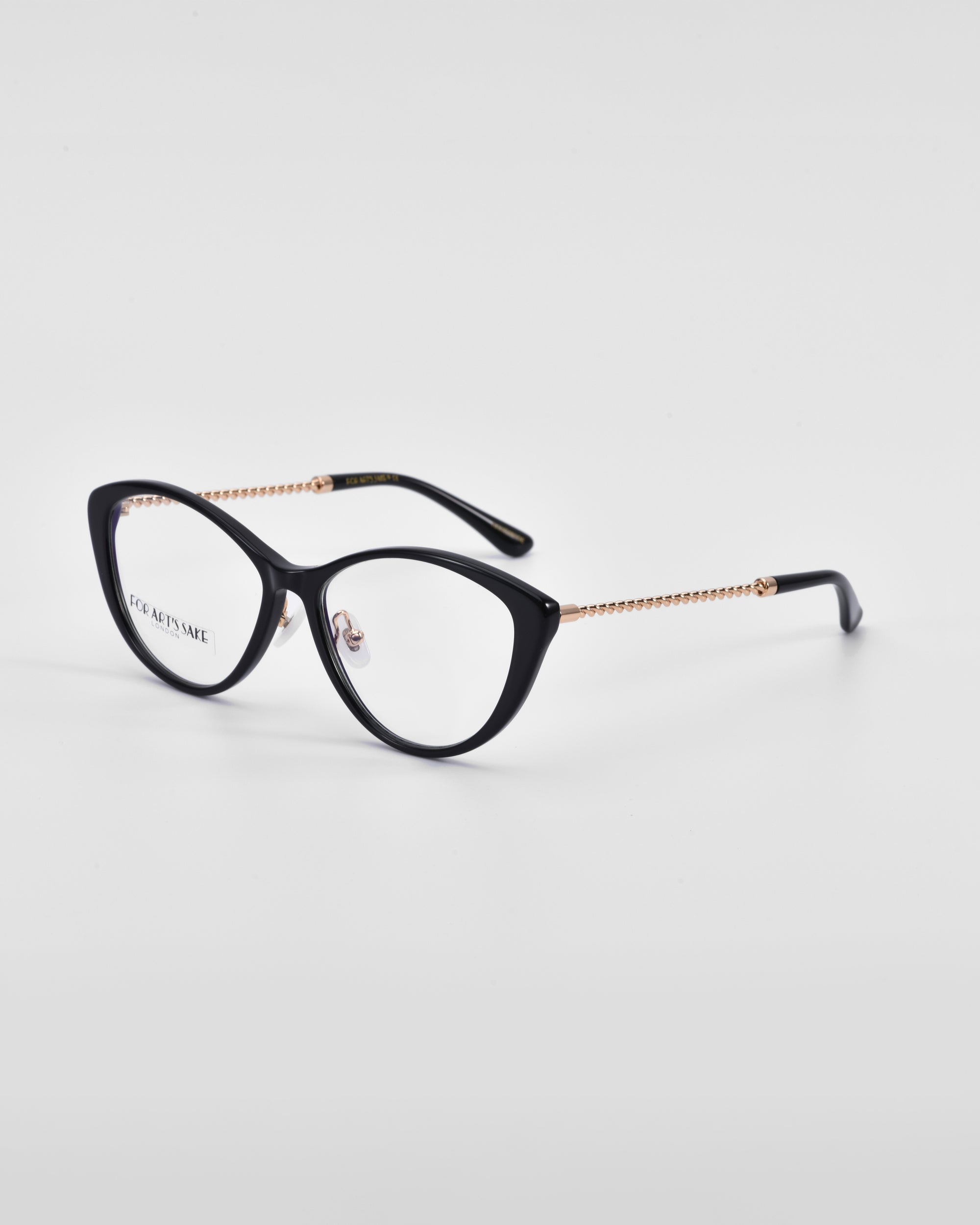 A pair of For Art&#39;s Sake® Perla II black cat-eye glasses with gold temple arms is placed on a white surface. The glasses have clear lenses, and the temple arms feature a beaded pattern and 18-karat gold plating, adding a touch of luxury to their optical design.
