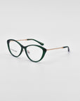 A pair of dark green Perla II eyeglasses with a cat-eye shape, positioned on a white background. The temples of the glasses are adorned with a gold chain-like pattern and 18-karat gold plating. The inside of the right lens is inscribed with "For Art's Sake®," highlighting their exquisite optical design.