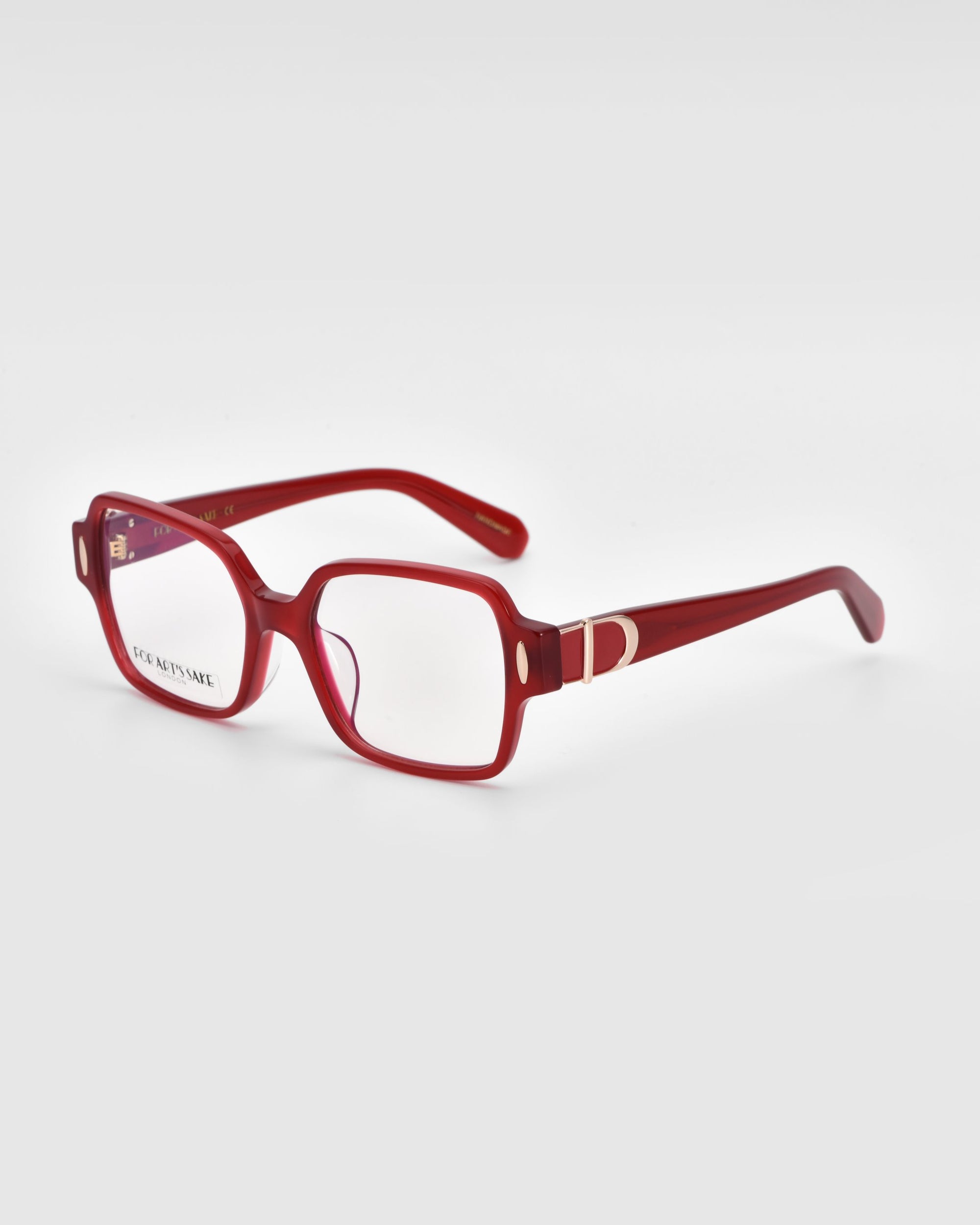 A pair of Hart eyeglasses by For Art&#39;s Sake®, featuring red rectangular frames with clear lenses and thick design. The temples boast a decorative silver accent near the hinges. These classic glasses are displayed on a white surface with the right temple extended outward.