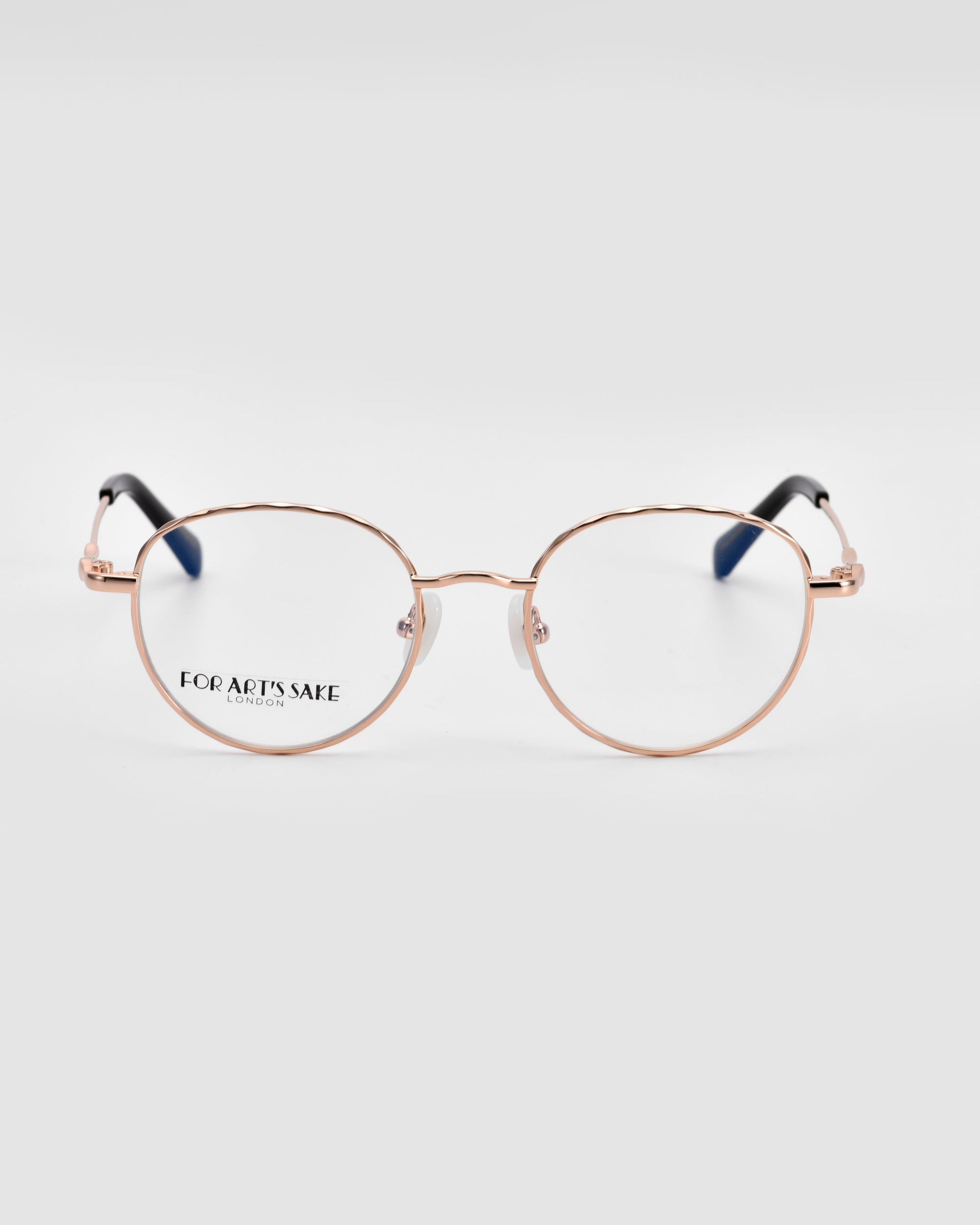 A pair of sleek round lenses in rose gold **Bone I** eyeglasses with luxurious metal detailing is centered in the image. The brand name "For Art's Sake®" is visible on the left lens. The background is plain white, making the glasses the focal point.