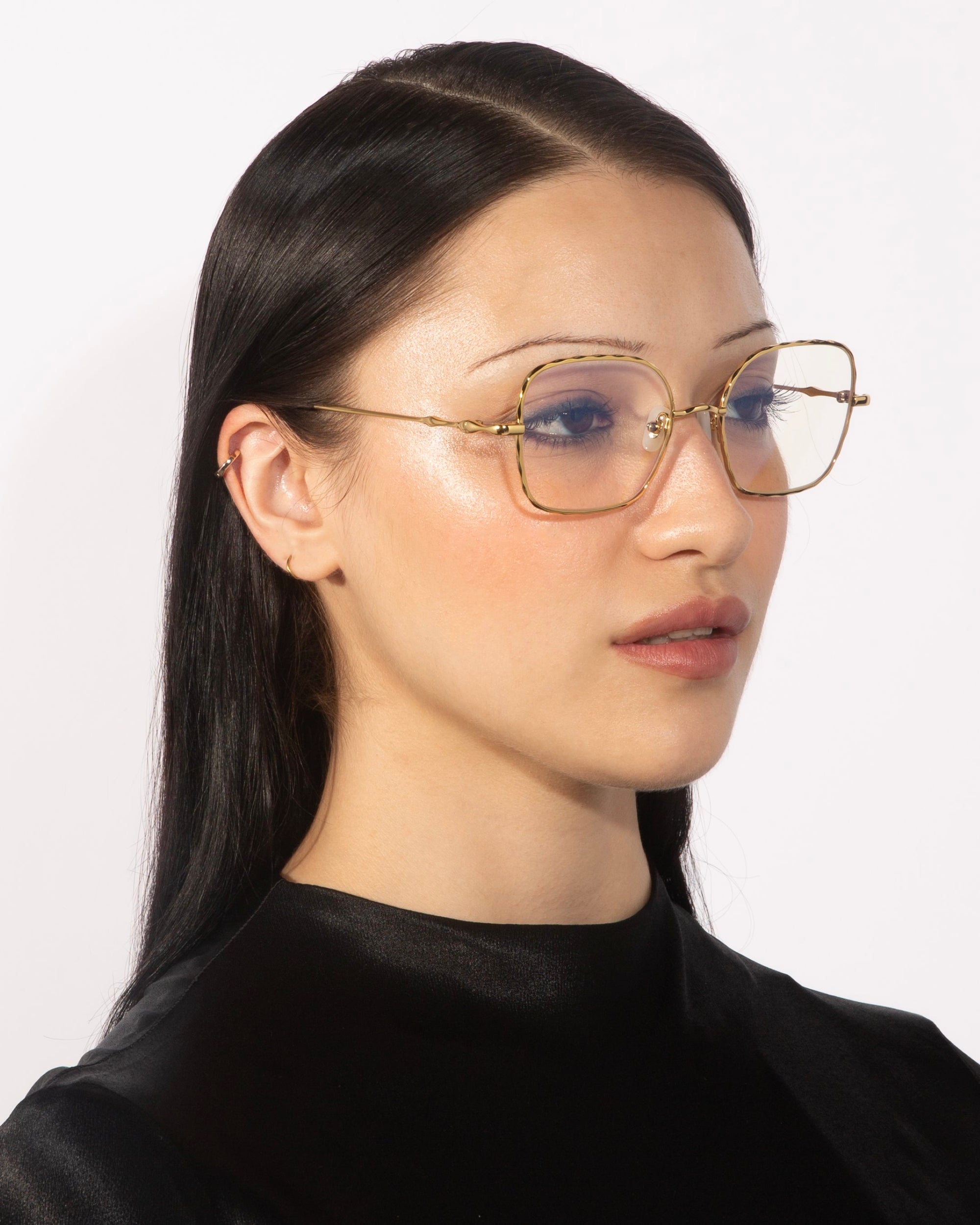 A woman with long, straight black hair wears elegant For Art&#39;s Sake® Bone II eyeglasses with clear lenses and jade nose pads. She has a subtle, natural makeup look and is dressed in a black top. The background is plain white.