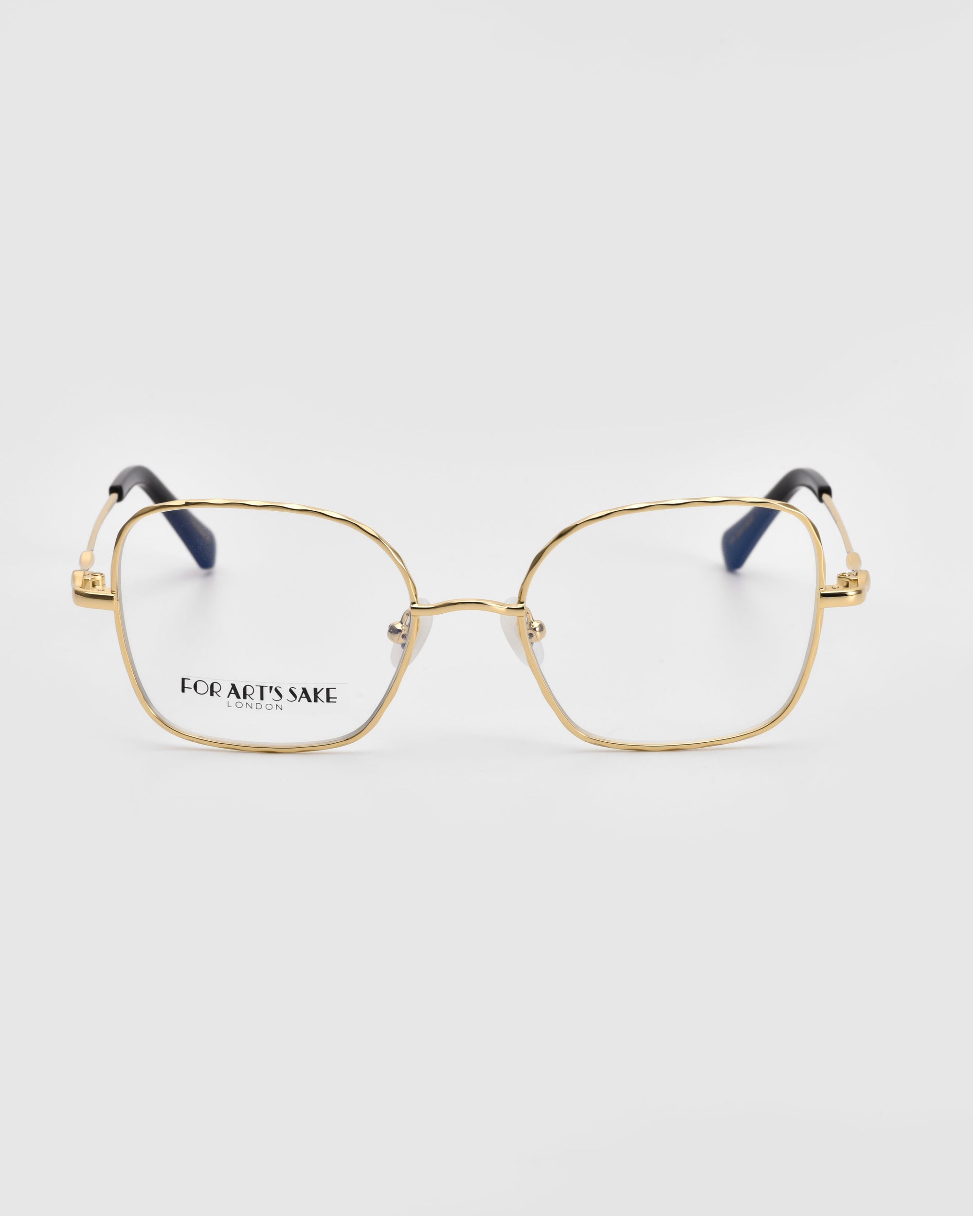 Introducing the Bone II by For Art&#39;s Sake®: a stylish pair of square-shaped eyeglasses featuring a delicate gold wireframe and dark temple tips. The lenses are subtly tinted, with &quot;FOR ART&#39;S SAKE&quot; elegantly displayed on the left lens. These exquisite glasses are showcased against a plain white background.