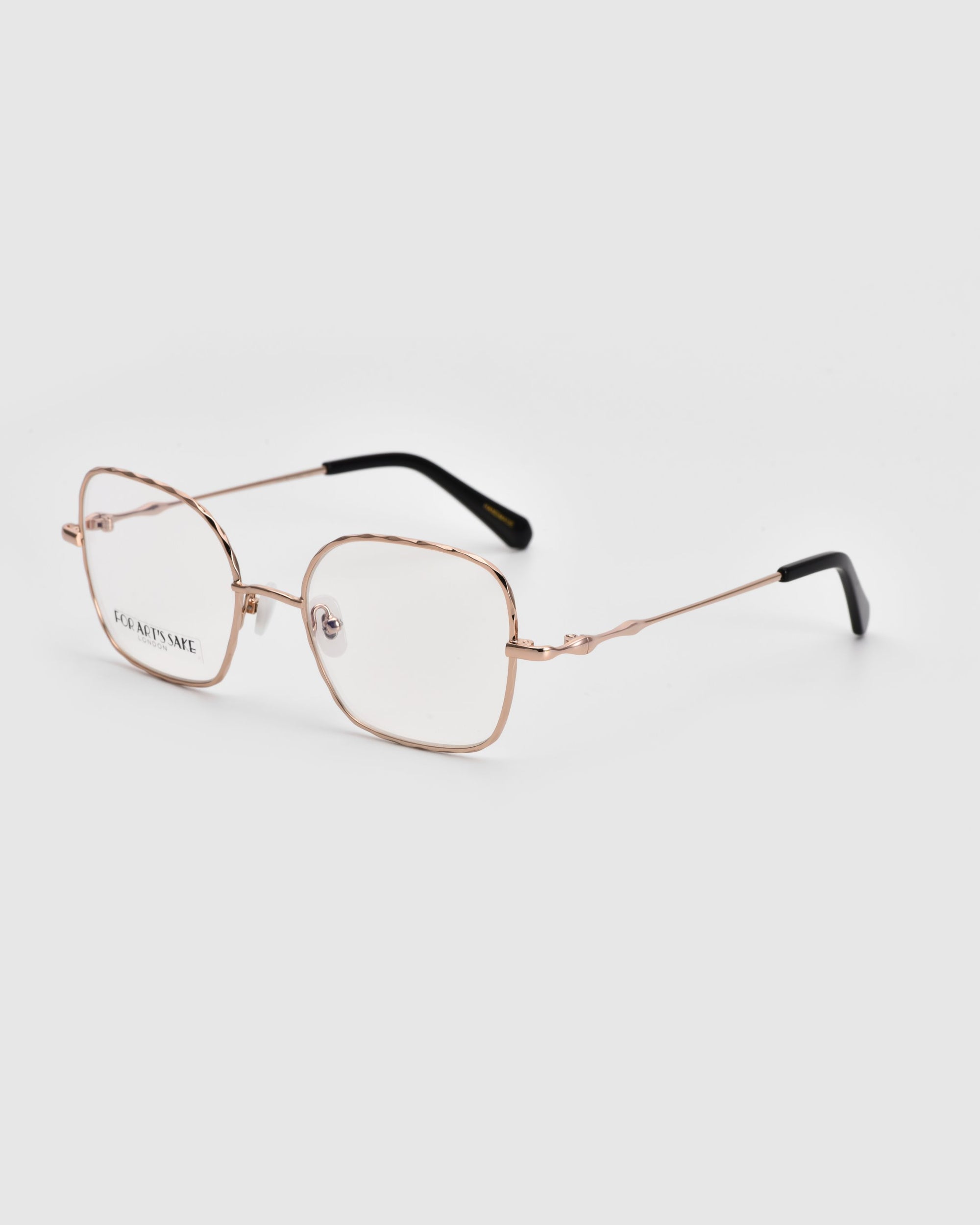 Introducing the Bone II from For Art&#39;s Sake®: a pair of eyeglasses with gold-colored metal frames. The slightly squared rectangular shape, complemented by black temple tips and transparent lenses, boasts a sleek wireframe construction. An elegant choice against the pristine white background.