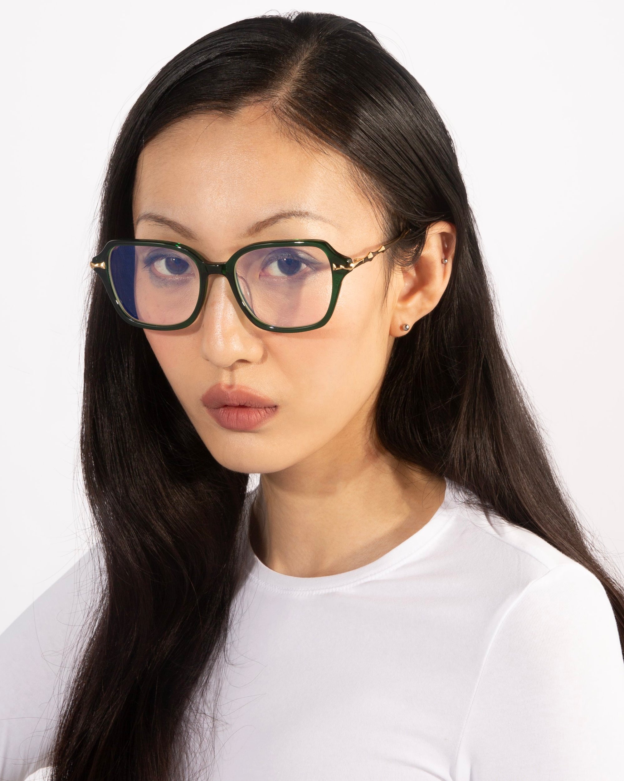 A person with long, dark hair wears Delight rectangular glasses with handcrafted frames from For Art&#39;s Sake®, paired with a white shirt, gazing directly at the camera against a plain white background.