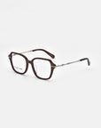 The "Delight" pair of square eyeglasses from For Art's Sake® boasts dark brown frames and long, thin temples. The temples feature a metallic section near the hinges, transitioning to a dark brown section at the ends. The clear lenses provide modern sophistication against a white background, evoking vintage charm.