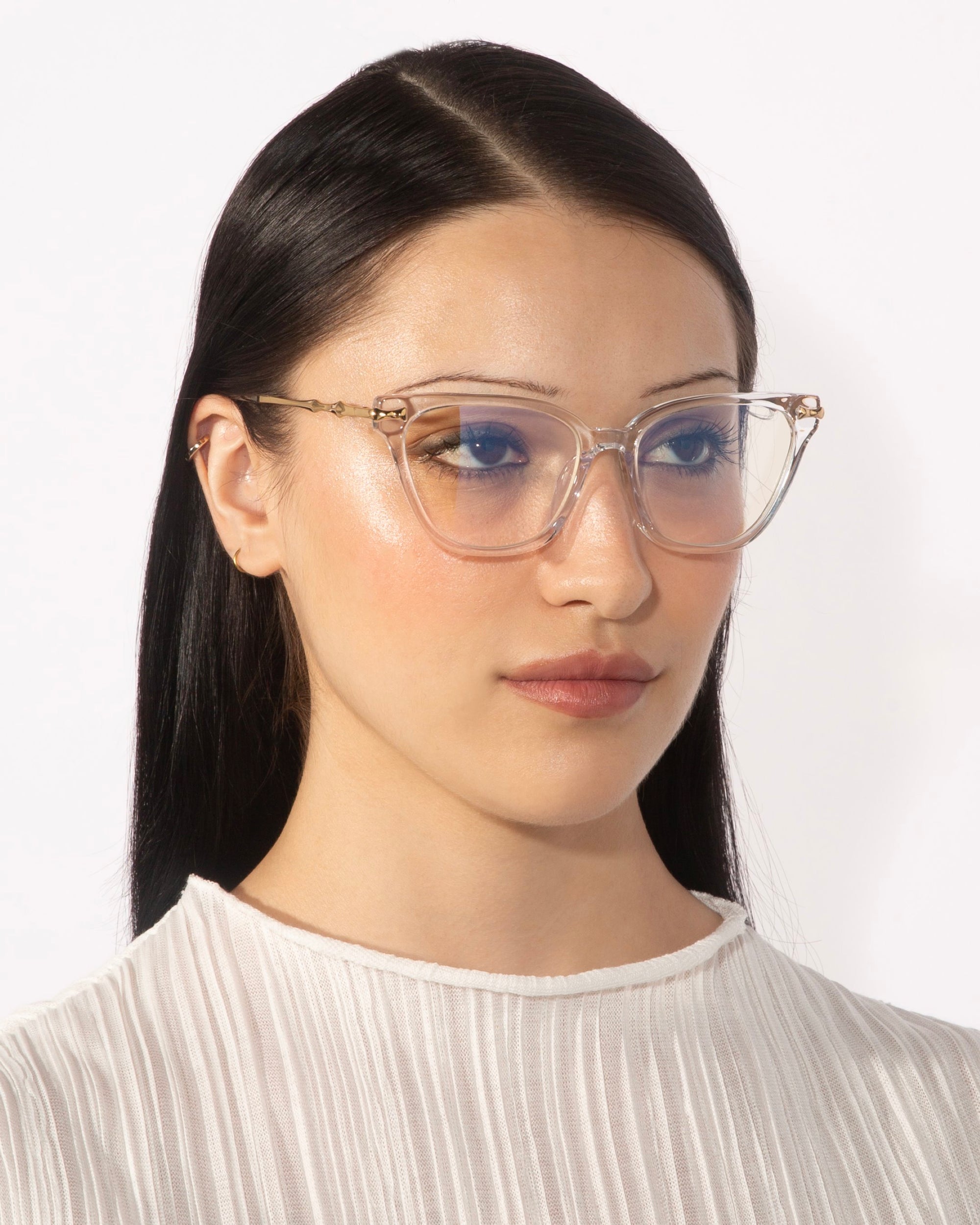 A person with long, straight dark hair is wearing the Lexie cat-eye frames by For Art&#39;s Sake® and a white pleated top. The background is plain white. The person has a neutral expression and is facing forward with a slight angle to the right.