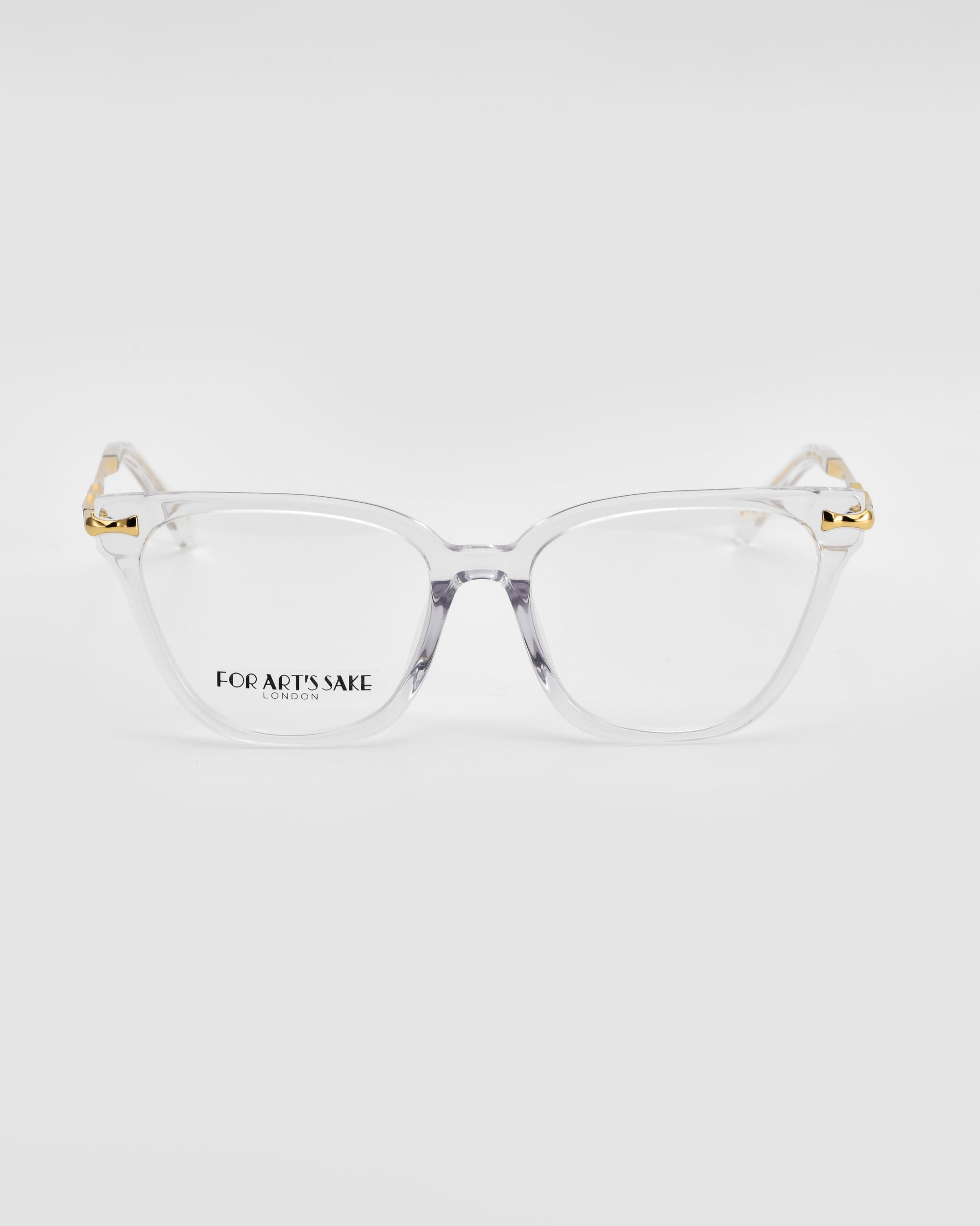 The Lexie eyeglasses from For Art&#39;s Sake® exude modern sophistication with their clear frames and gold-accented hinges. Featuring transparent lenses with &quot;FOR ART&#39;S SAKE LONDON&quot; printed on the left lens, these glasses are displayed against a white background, offering a subtle touch of vintage charm to any ensemble.