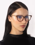 A woman with straight, dark hair and fair skin is wearing the Lexie cat-eye frames from For Art's Sake® that exude vintage charm. She looks slightly to the side with a neutral expression, set against a plain white background.