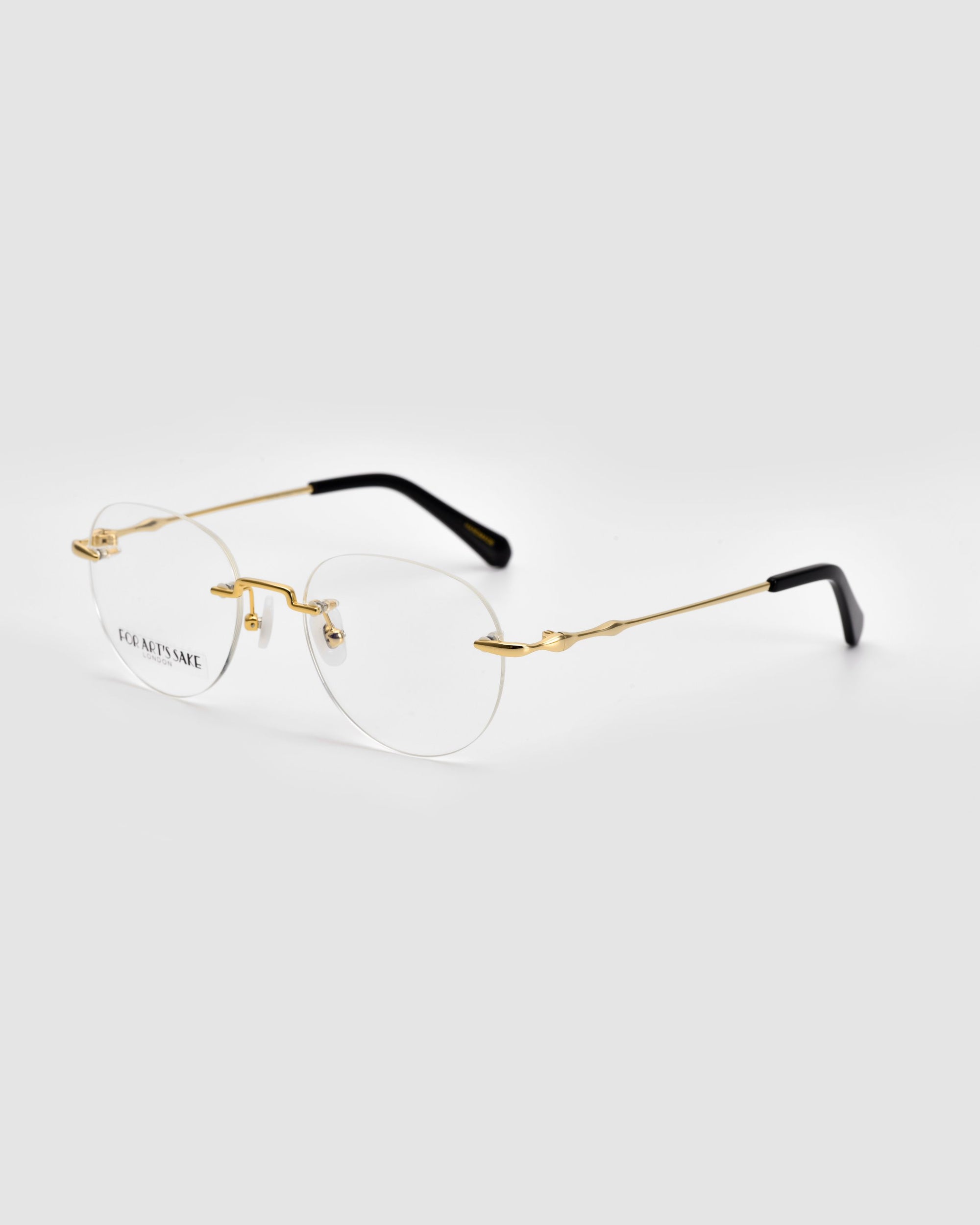 The Misty eyeglasses by For Art&#39;s Sake® feature a pair of rimless lenses with gold-toned metal temples and bridge, complemented by black earpieces. These glasses boast an elegant and minimalistic design with their rectangular lenses and sleek, modern wireframe construction set against a plain white background.