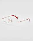 The Misty by For Art's Sake® features a pair of rimless eyeglasses with round lenses, gold-tone metal arms, and red tips on the ends of the temples. The minimalist and lightweight wireframe construction offers a clear and modern aesthetic against a white background.