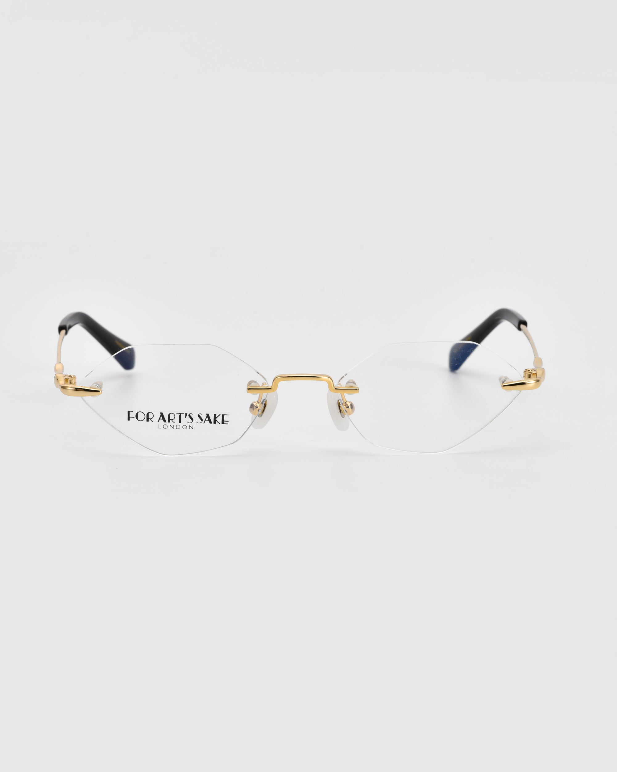 A pair of sleek, rimless Zesty eyeglasses with thin, gold-colored temples and nose bridge from For Art&#39;s Sake®. The tips of the temples are black. The lightweight optical glasses rest on a white background and have &quot;FOR ART&#39;S SAKE LONDON&quot; printed on the left lens.