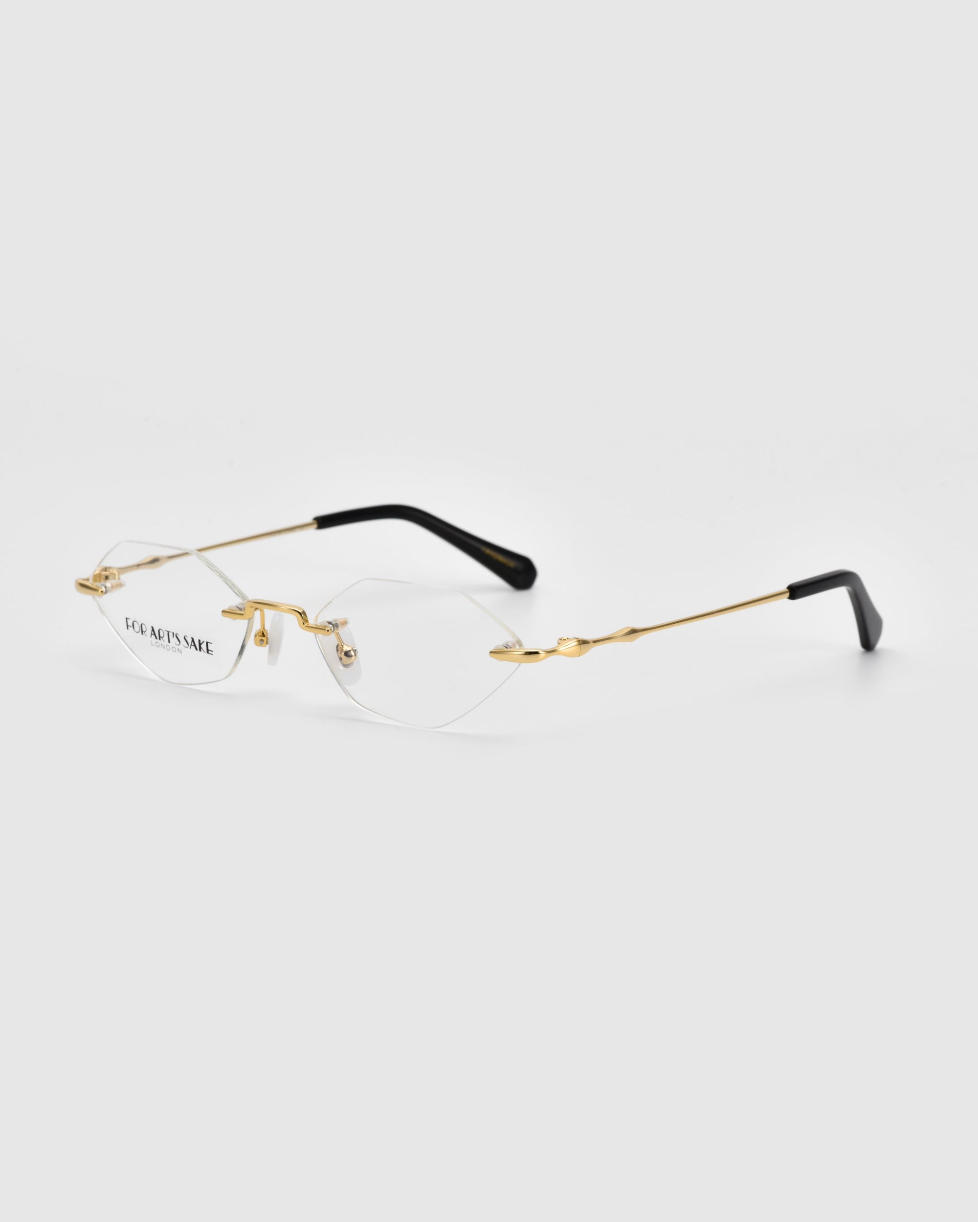 A pair of rimless eyeglasses with gold-colored temples and black tips, identified by the product name "Zesty" from the brand For Art's Sake®, is shown against a plain white background. The clear lenses and visible nose pads contribute to a sleek, minimalist design embracing modern minimalism. The lightweight eyewear also features the brand name "For Art's Sake®" printed on one lens.