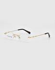 A pair of rimless eyeglasses with gold-colored temples and black tips, identified by the product name "Zesty" from the brand For Art's Sake®, is shown against a plain white background. The clear lenses and visible nose pads contribute to a sleek, minimalist design embracing modern minimalism. The lightweight eyewear also features the brand name "For Art's Sake®" printed on one lens.