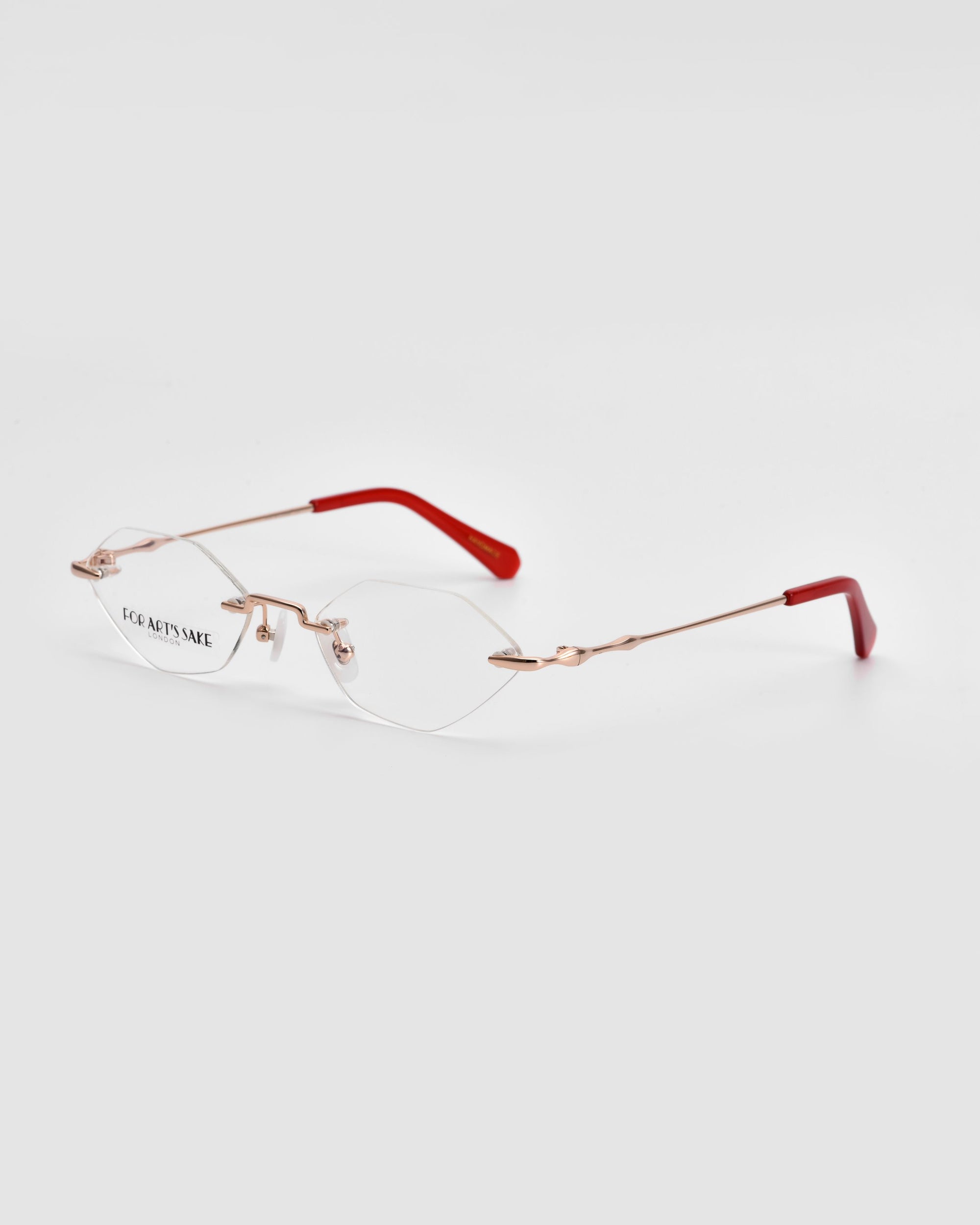 The &quot;Zesty&quot; glasses by For Art&#39;s Sake® are a stylish pair of frameless optical eyewear, featuring gold-tone temples and red temple tips. With a modern minimalist design and clear lenses that display the words &quot;FOR ART&#39;S SAKE,&quot; these lightweight glasses are perfectly showcased against a plain white background.