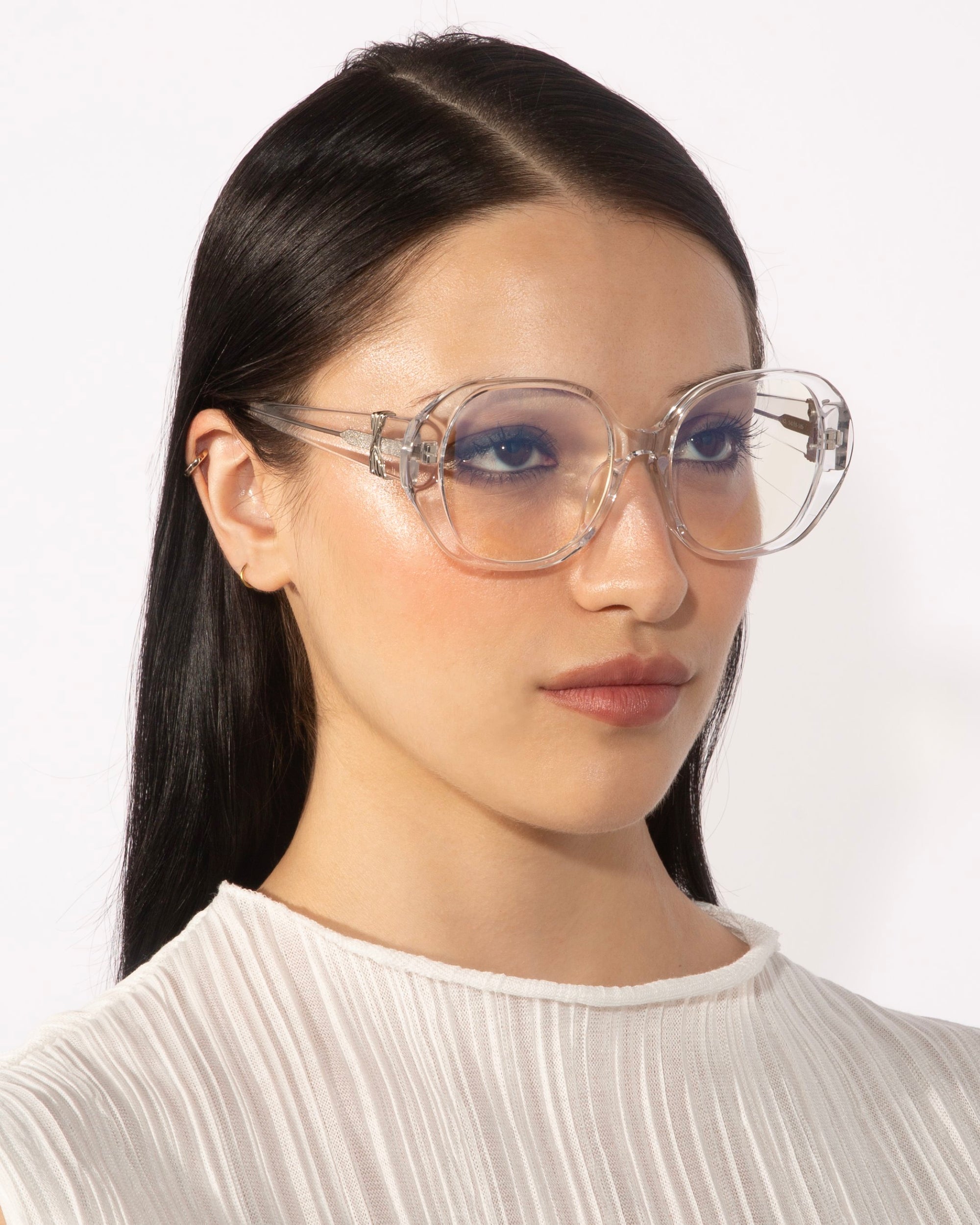 A person with long, straight black hair is wearing the For Art&#39;s Sake® Bow eyeglasses, which feature large, transparent lenses and a unique vintage design. The individual has a serious expression and is dressed in a white, textured high-neck top against a plain white background.