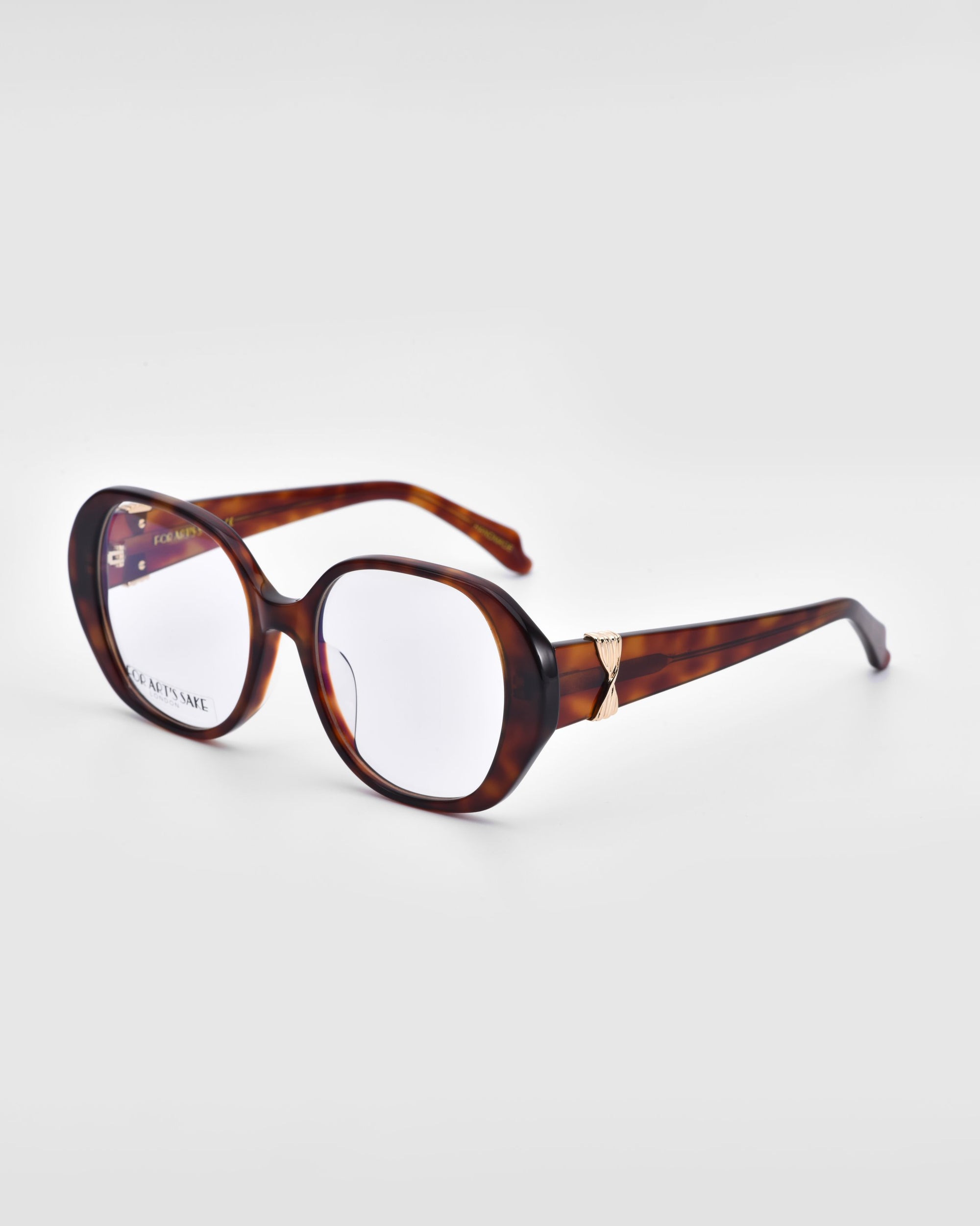 A pair of bold and stylish Bow tortoiseshell eyeglasses from For Art's Sake®, featuring thick, rounded frames with clear lenses, positioned at an angle on a plain white surface. The arms of the glasses showcase a subtle gold accent near the hinges.