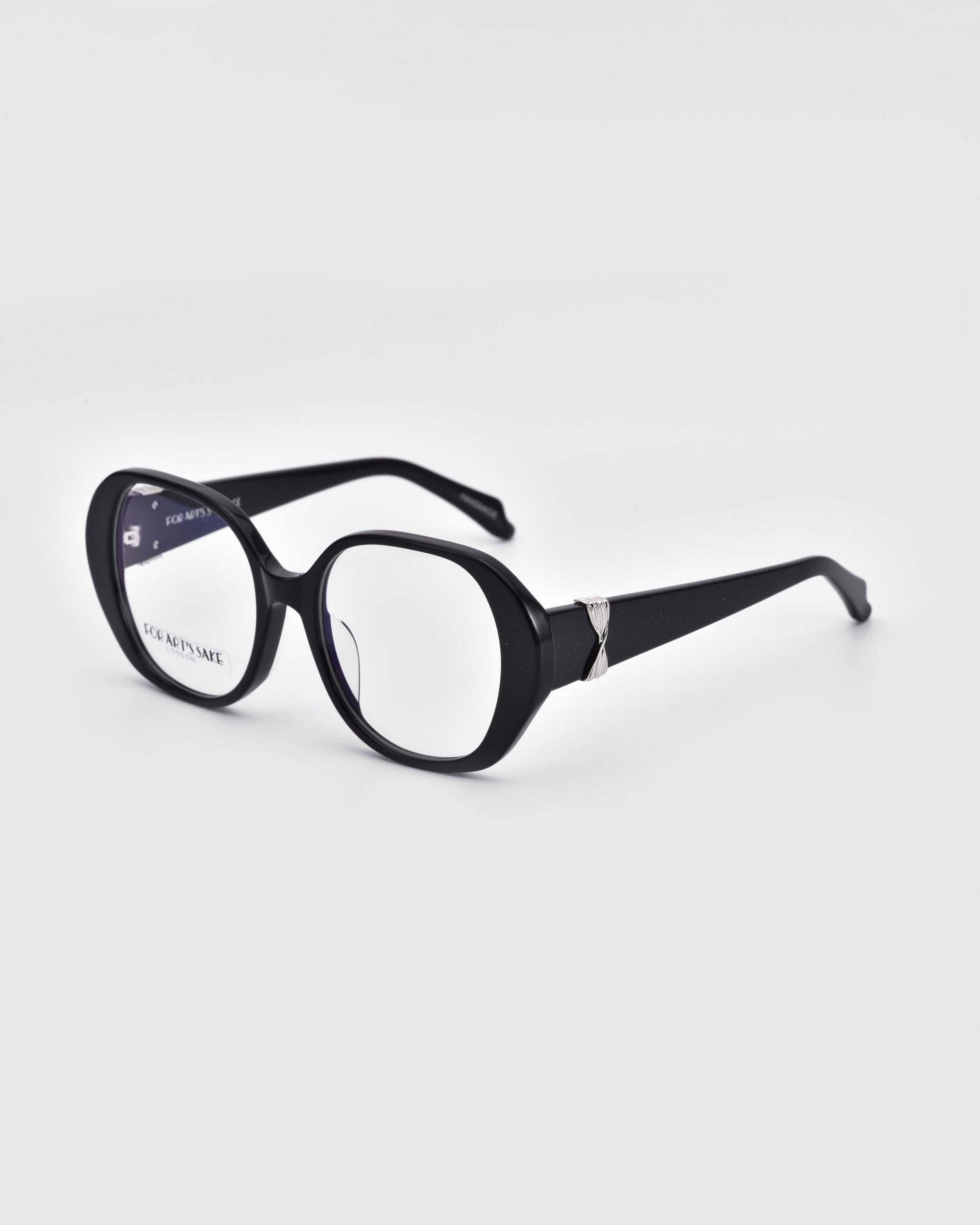 The Bow glasses from For Art's Sake® are showcased against a white backdrop, featuring bold and stylish oversized black rectangular lenses. The thick frames and temples, made from biodegradable acetate, are adorned with a decorative silver accent near the hinges.