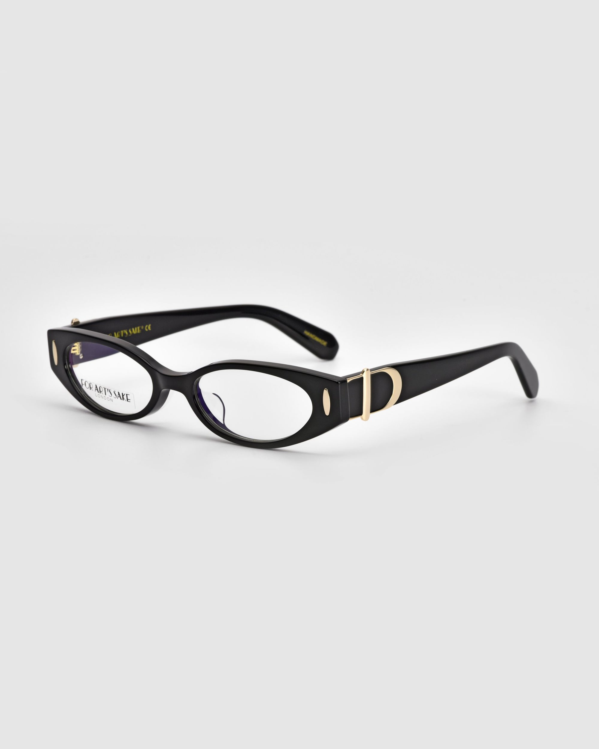 The Cigar eyeglasses by For Art&#39;s Sake® are a pair of stylish black frames with a sleek design, featuring small circular cutouts near the hinges and golden accents on the polished acetate temples. The lenses have a slightly oval shape, evoking vintage charm, while the interior of the arms is embossed with brand information.