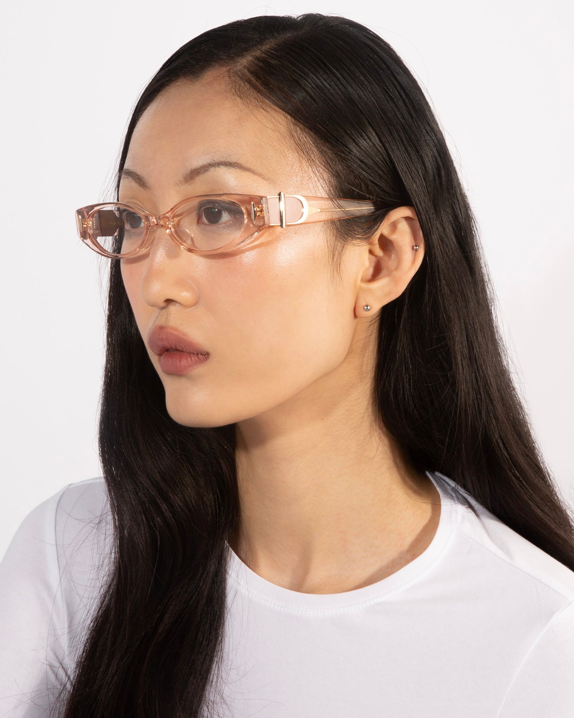 A person with long, straight hair and wearing transparent pink For Art&#39;s Sake® Cigar frames looks to the side. They are dressed in a white top, exuding a serene expression. The background is plain white, adding a contemporary edge to the scene.