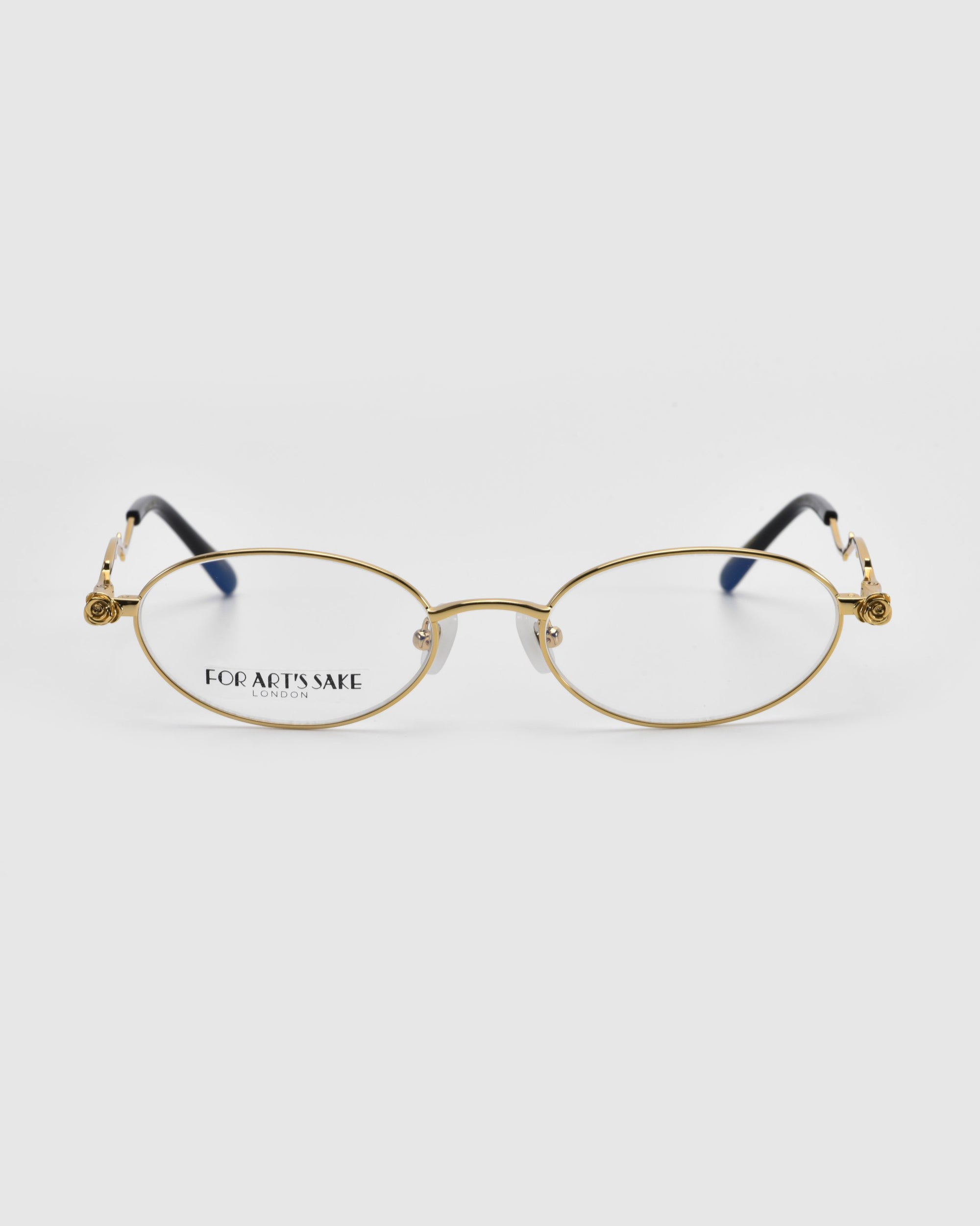 Gold-framed oval eyeglasses from the Rose Garden collection, named Thorn by For Art's Sake®, feature black temple tips. Displayed on a white background, the left lens displays “FOR ART’S SAKE” in black, exemplifying elegance and design innovation.