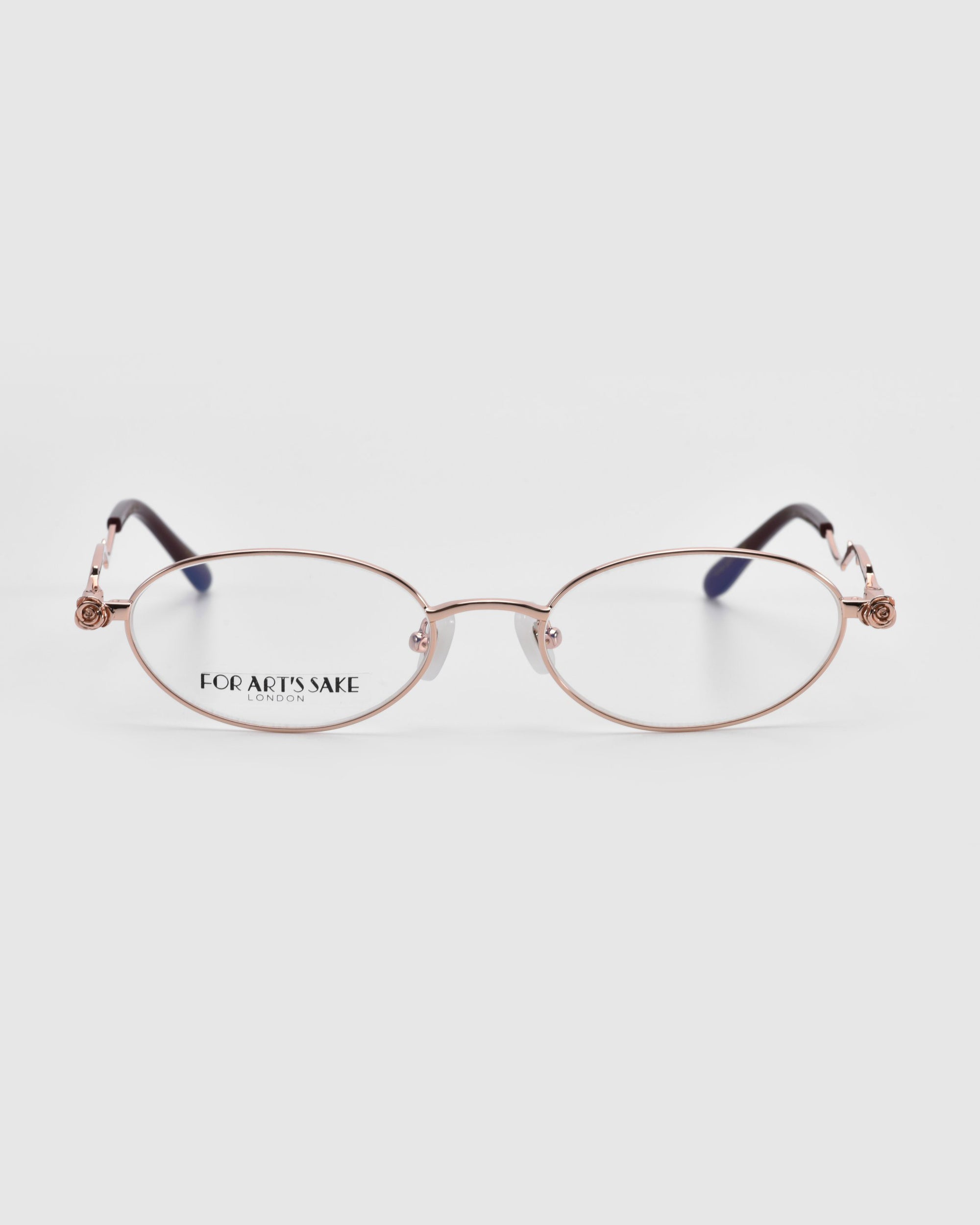 These Thorn optical eyeglasses from For Art's Sake® feature thin, oval gold frames with black temple tips. Set against a light grey background, they epitomize artistic expression in a chic design and proudly display the brand name on the left lens.