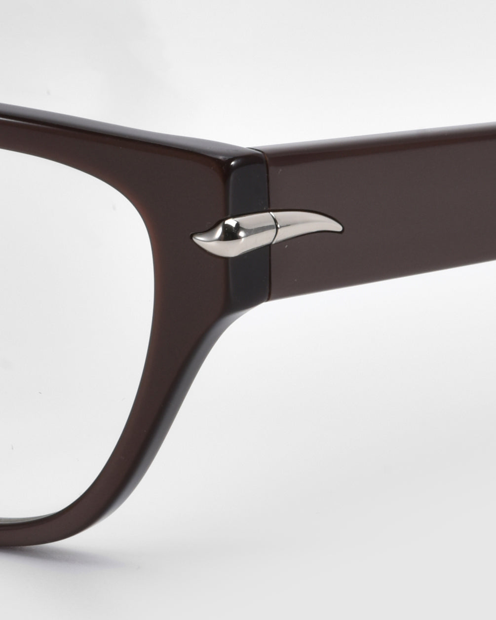 Close-up of For Art's Sake® Eros cat-eye acetate frames in brown, featuring a silver accent on the temple hinge. These chic sunglasses offer a sleek and modern look against a light gray background, making them perfect for everyday wear.