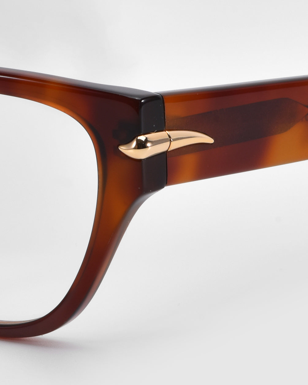 Close-up of the Eros eyeglass frames by For Art's Sake®. These brown, rectangular frames feature a unique gold metallic horn-shaped detail on the hinge against a plain white background, highlighting their elegant design.