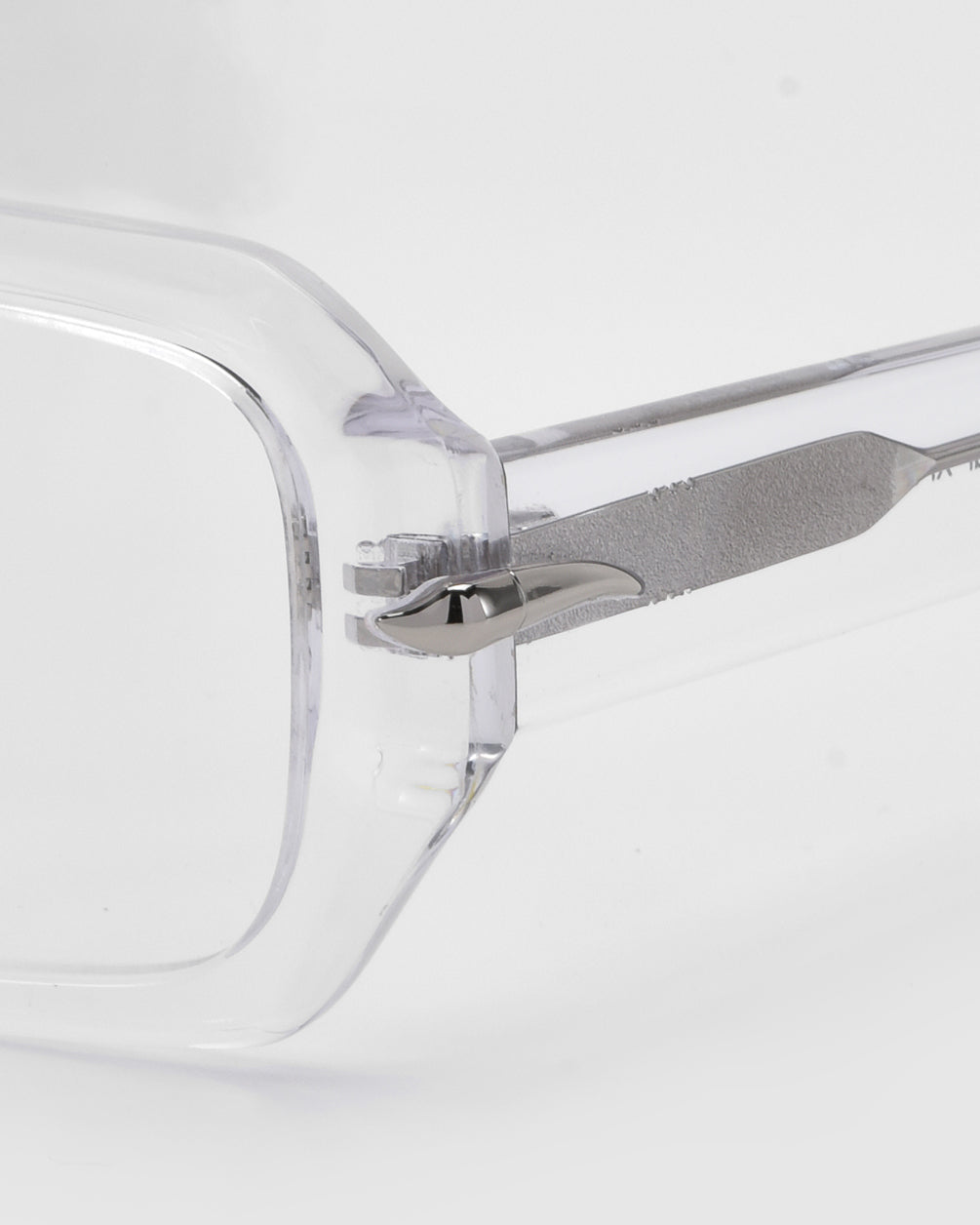 Close-up of For Art&#39;s Sake® Petal eyeglasses featuring a clear rectangular frame and minimalist design. The image highlights the connection between lens and arm, showcasing the metal hinge detail against a neutral background, providing a versatile style for any look.