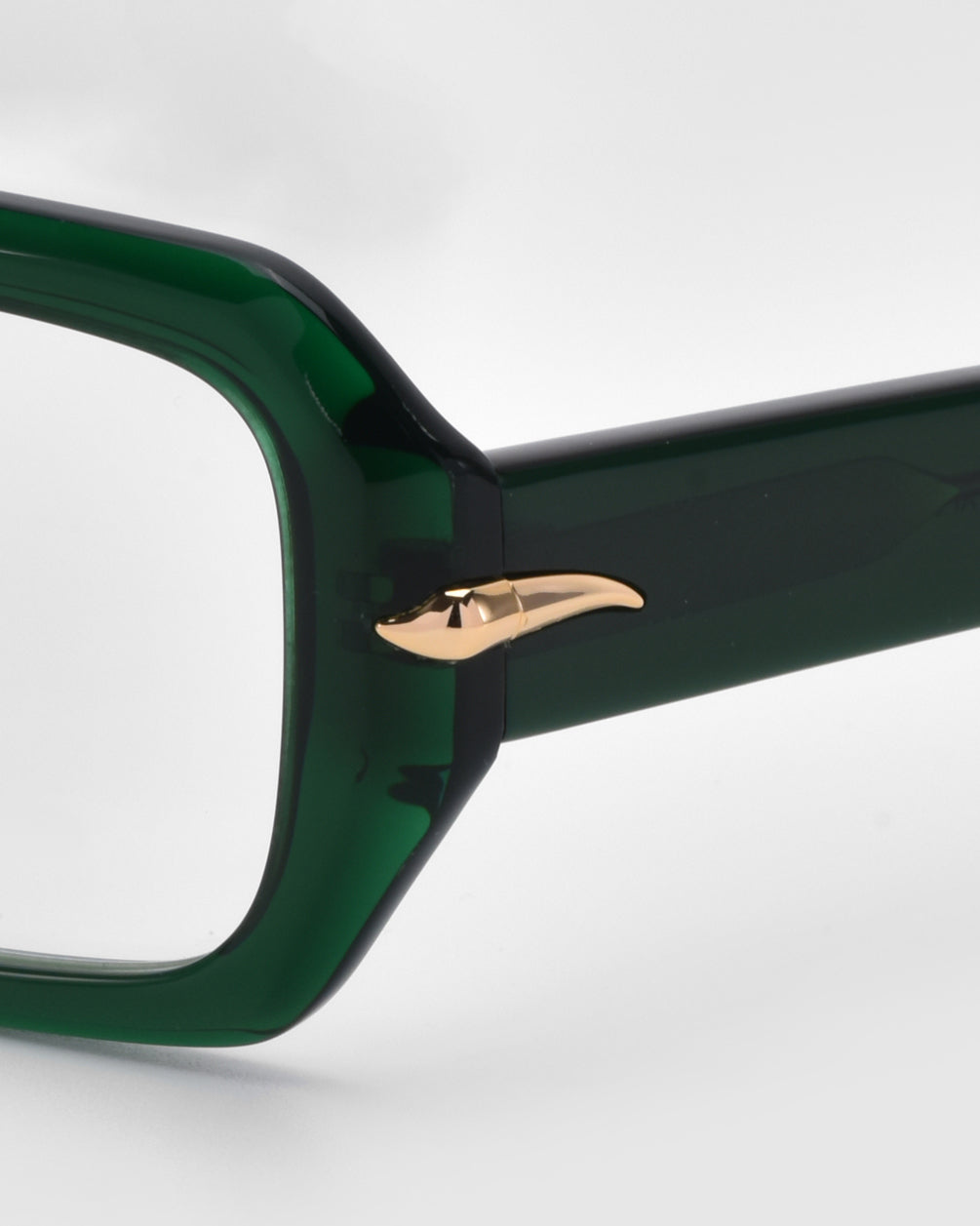 A close-up of For Art&#39;s Sake® Petal eyeglasses highlights their minimalist dark green frame with a small gold chili pepper accent on the corner, set against a light background.