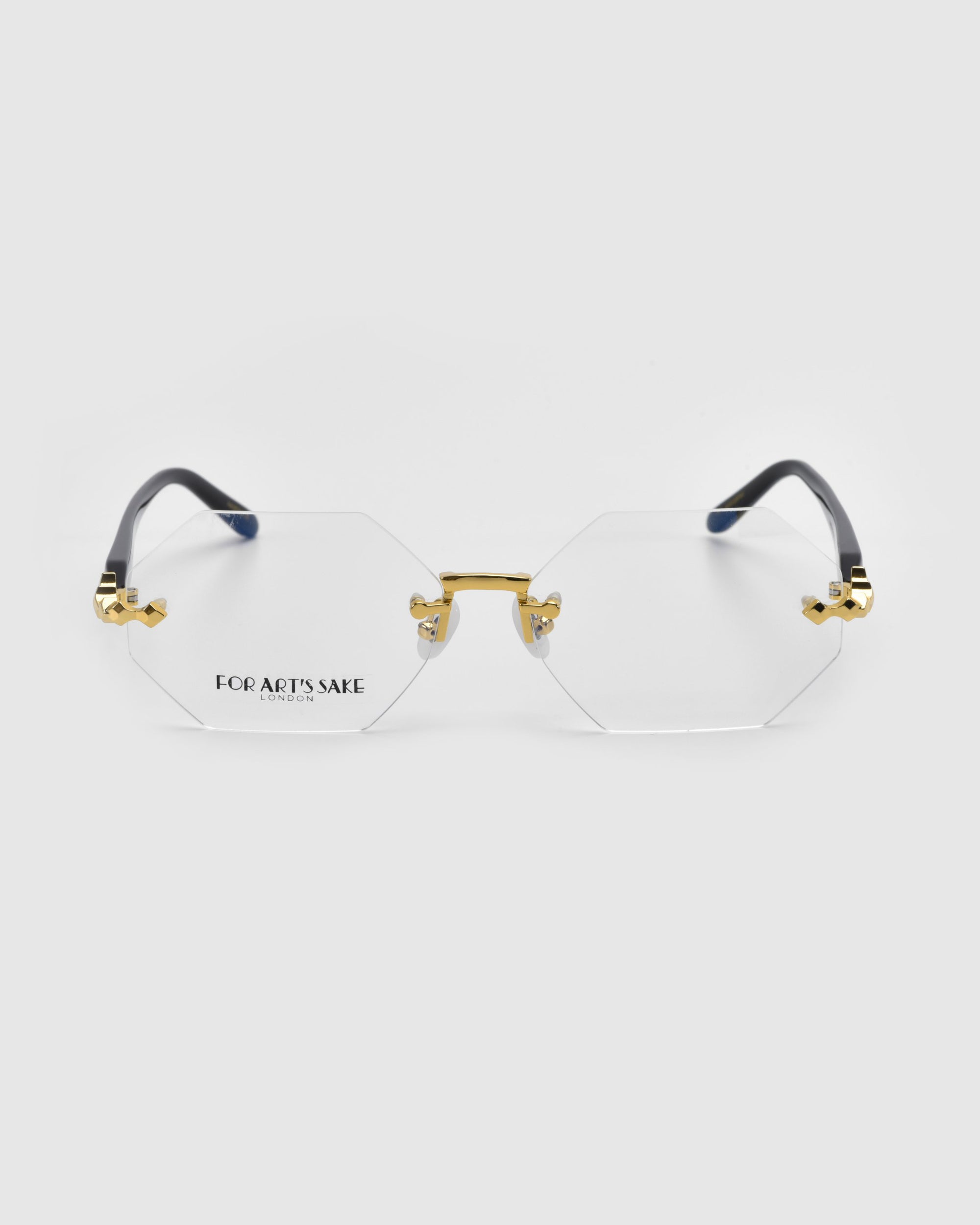 The Hampton from For Art&#39;s Sake® is part of the Rose Garden collection, featuring octagonal eyeglasses with clear lenses, gold-toned frames on a white backdrop, and sleek black temples. The brand name is subtly visible on one lens.