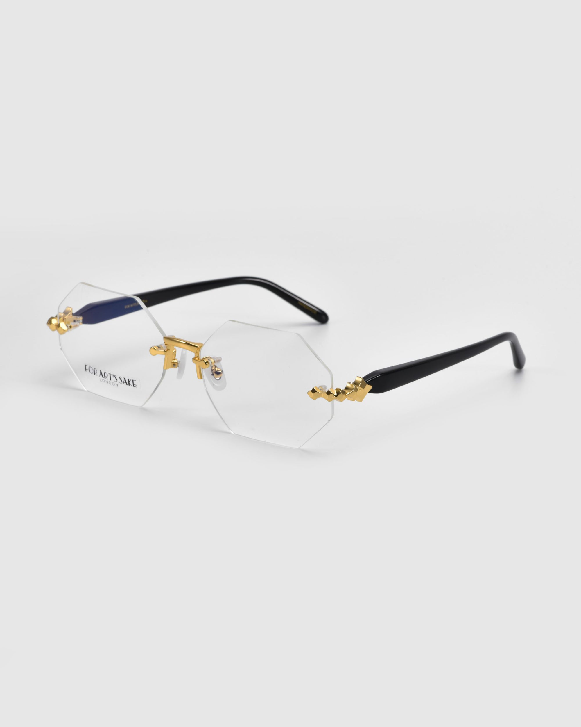 Hampton hexagonal eyeglasses by For Art's Sake® showcase clear lenses, thin gold rims, and black temples. Part of the Rose Garden collection, they feature decorative gold accents on the bridge and temple tips for a stylish modern look.