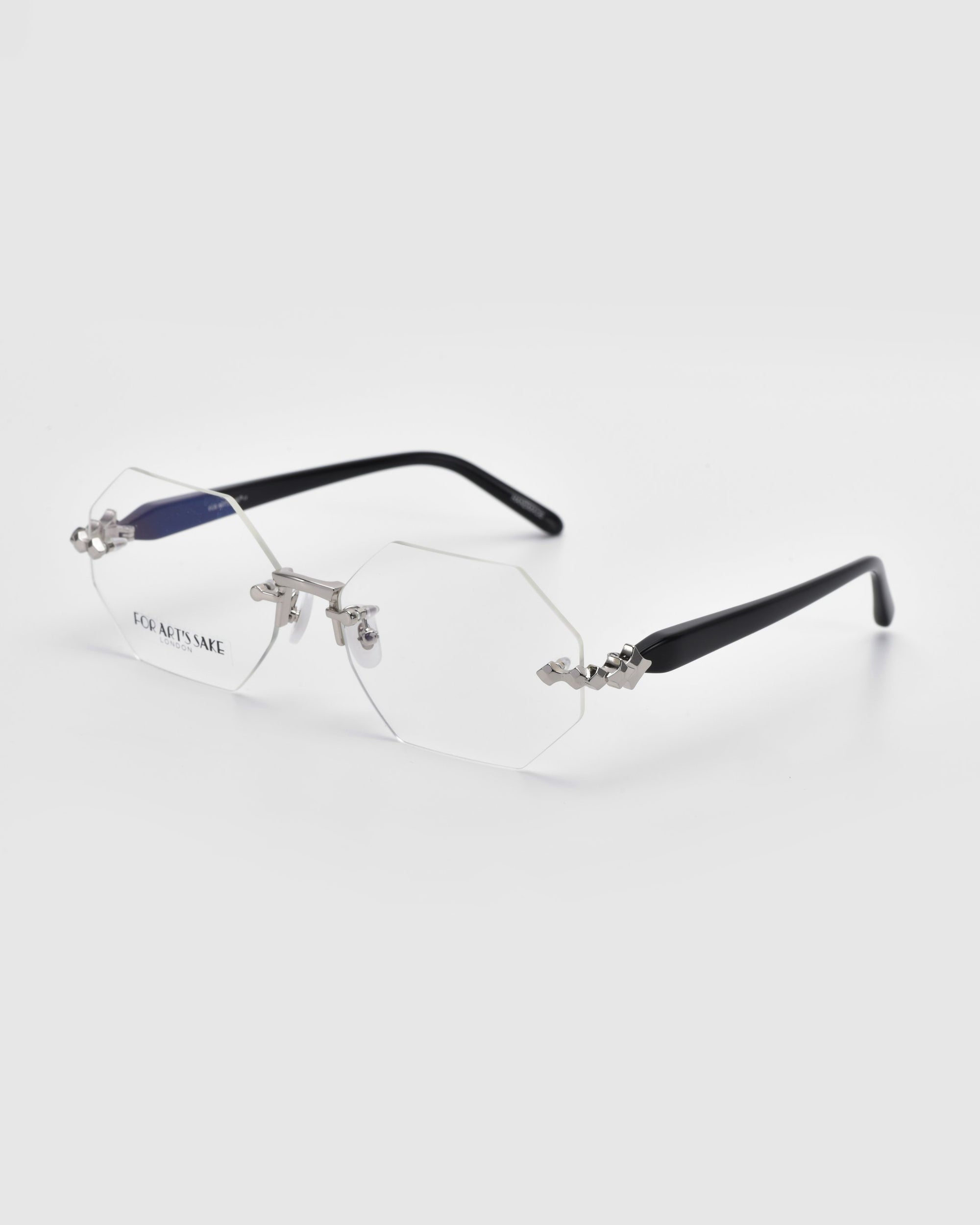 The Hampton eyeglasses from For Art&#39;s Sake® feature a hexagonal, rimless design with black temple arms against a plain white background. The lenses have metal accents at the hinges, with &quot;For Art&#39;s Sake&quot; subtly visible on one lens.