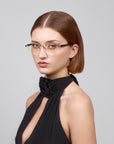 A woman with short brown hair and soft rectangular lenses by For Art's Sake® wears the Claremont, a black halter dress with a floral neck detail from the Rose Garden collection. She stands against a plain light backdrop, looking slightly aside with a neutral expression.