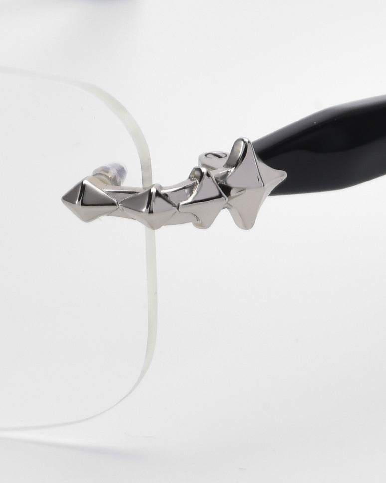 Close-up of the side of For Art's Sake® Claremont eyewear, showcasing a unique silver star design on the black temple arm. Rectangular lenses with curved edges are attached to the decorative hinge against a plain white background.