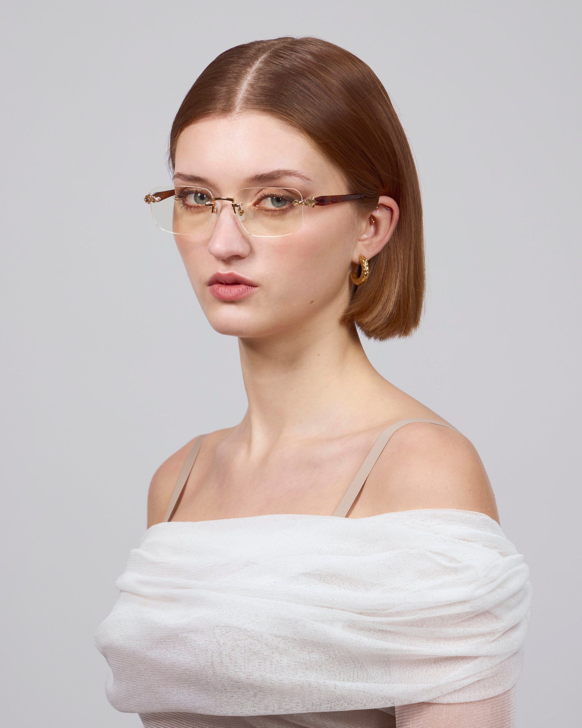 Someone with straight brown hair and glasses is wearing a Claremont light off-shoulder top by For Art's Sake®. The plain light gray background complements this timeless classic look.