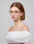 Someone with straight brown hair and glasses is wearing a Claremont light off-shoulder top by For Art's Sake®. The plain light gray background complements this timeless classic look.