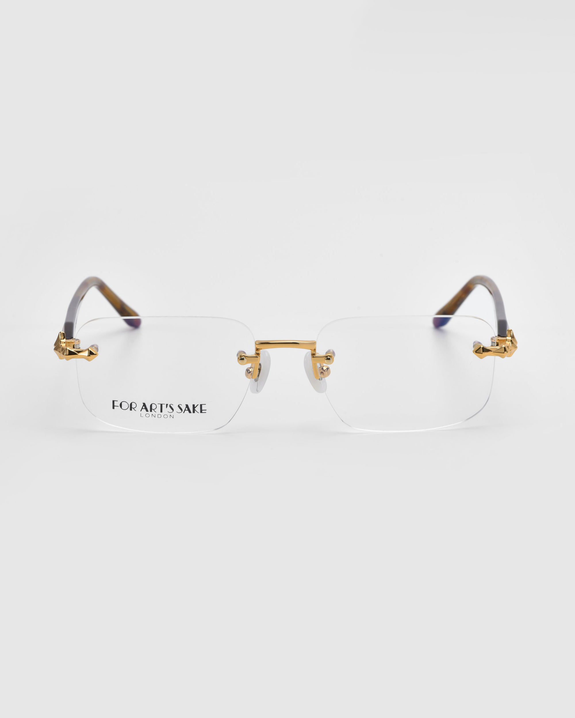 The Claremont rimless eyeglasses feature gold-toned metal details, clear lenses, and brown temple tips from the Rose Garden collection by For Art's Sake®, with a timeless classic look set against a white background.