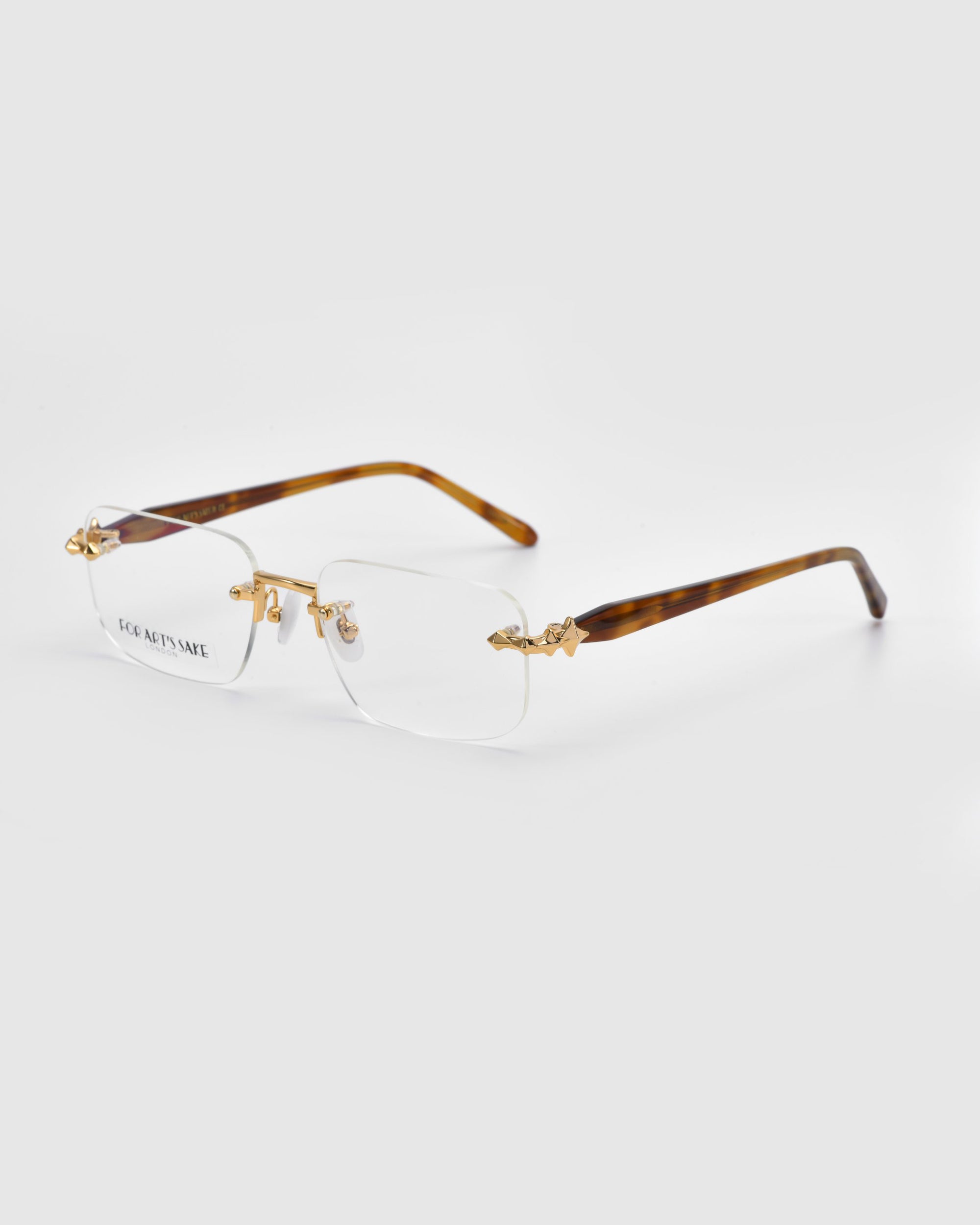 As part of the Rose Garden collection, Claremont rimless eyeglasses from For Art's Sake® feature rectangular lenses with gold temple detailing and clear surfaces. The brown arms showcase a tortoiseshell pattern, and the brand name appears on the lens against a light gray background.