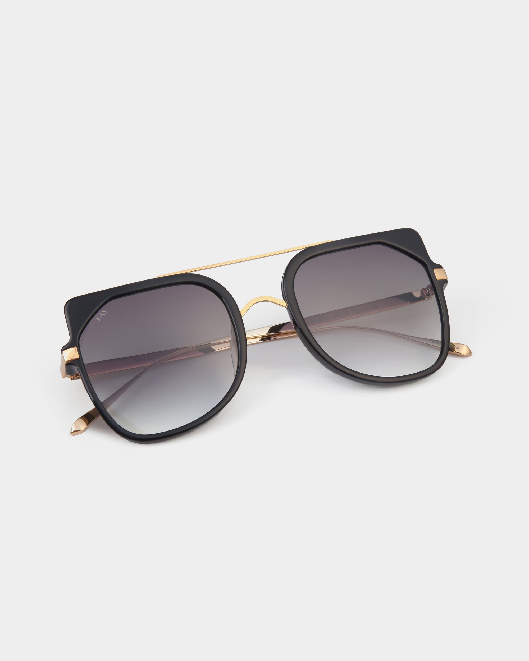 A pair of stylish For Art&#39;s Sake® Big Game aviator sunglasses with large black square frames, gold accents, and dark tinted lenses rests on a white background. These sunglasses feature a double-bridge design, with one bridge in gold, adding an extra touch of elegance while providing UV protection.