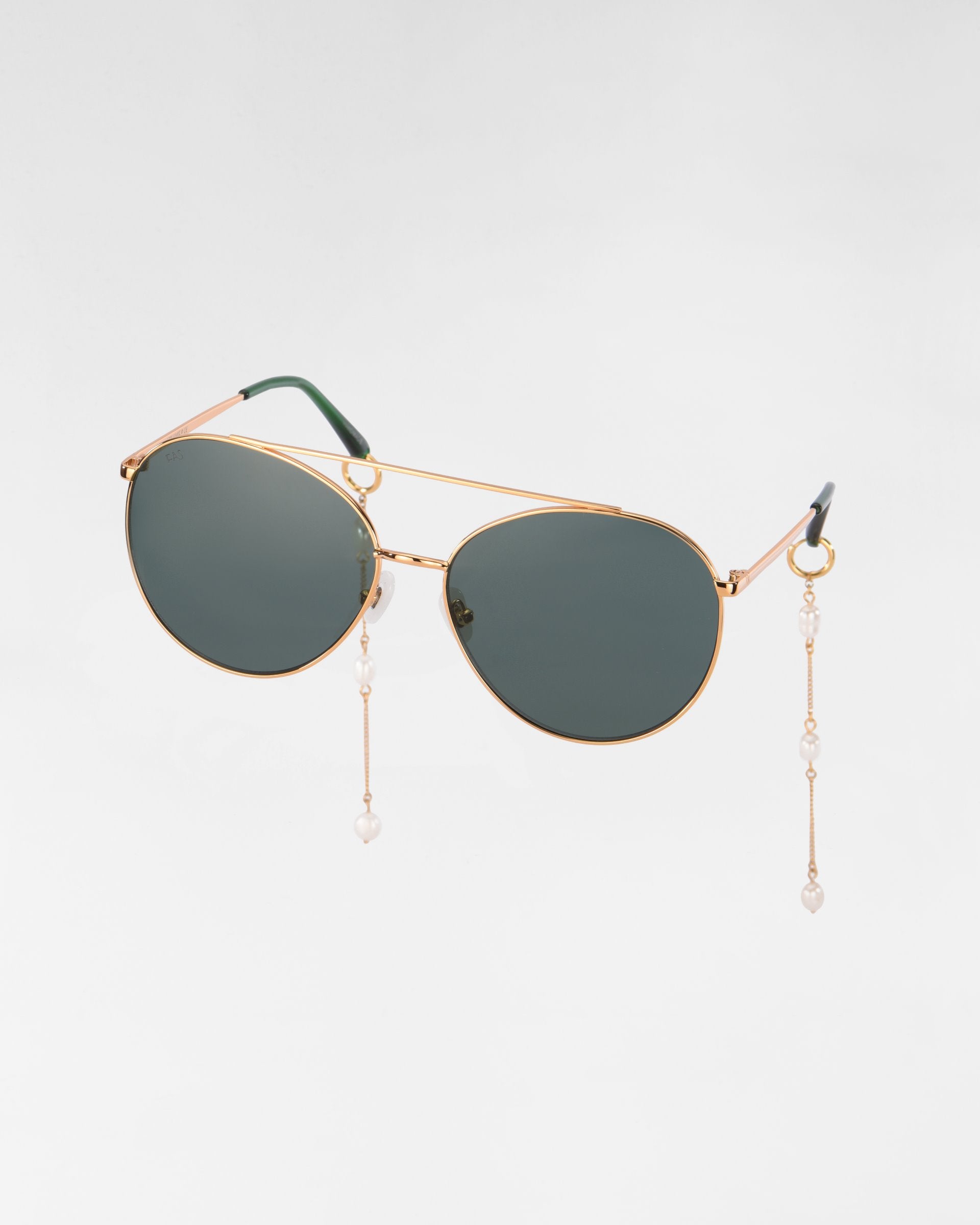 A pair of Yoyo sunglasses by For Art&#39;s Sake® with dark lenses and 18k gold-plated frames. The sunglasses feature decorative chains with small freshwater pearls hanging from the temples. The background is plain white.