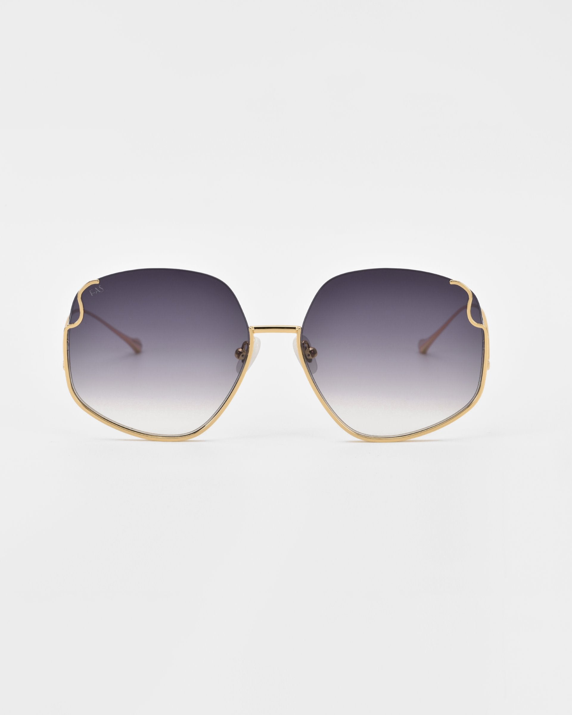 A pair of luxurious For Art&#39;s Sake® Drape sunglasses with gold frames and large, slightly hexagonal lenses. The lenses have a gradient tint, transitioning from dark at the top to lighter at the bottom. The frame features intricate metal detailing on thin arms and a minimalistic design. The background is plain white.