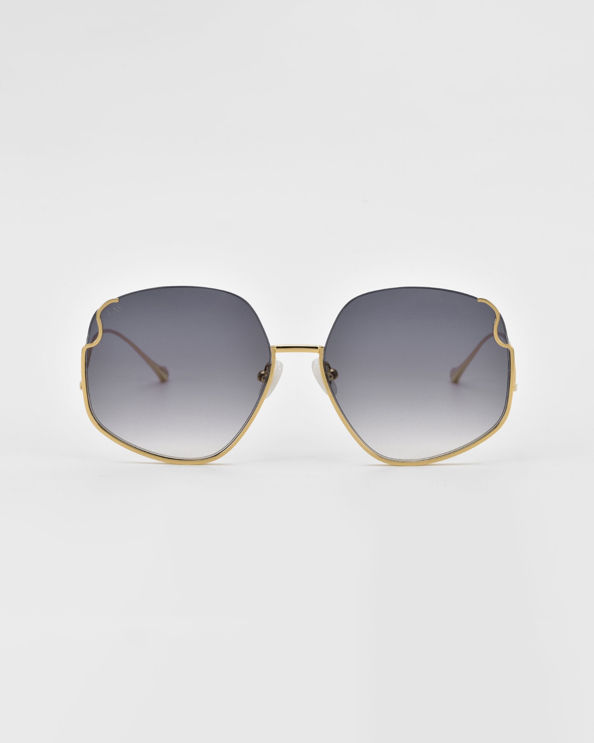 A pair of For Art&#39;s Sake® Drape sunglasses with large, hexagonal lenses featuring a gradient tint from dark grey to light grey. The sunglasses have a thin, gold metal frame with intricate metal detailing and delicate gold temples. The background is a plain, soft white.